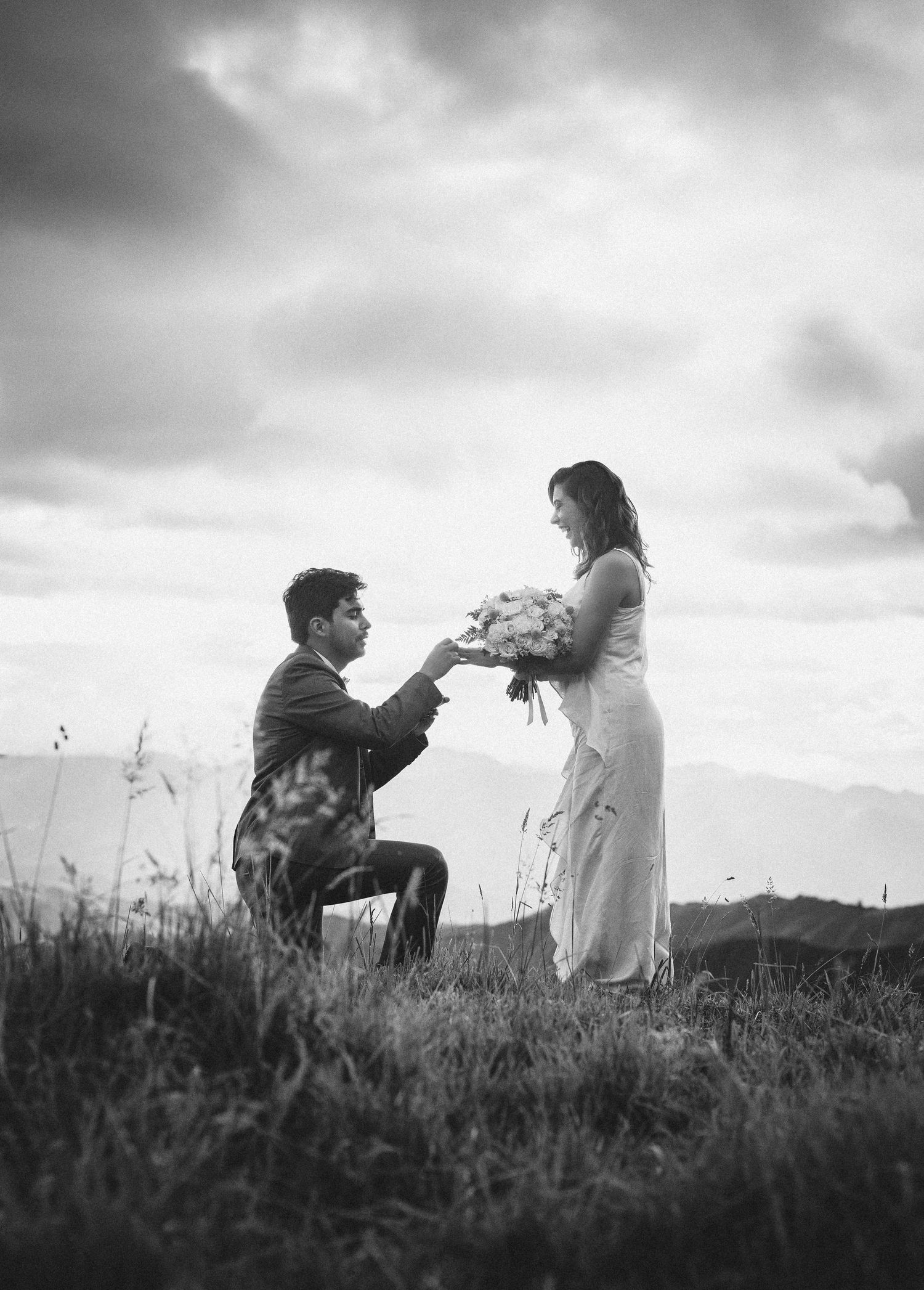 A romantic marriage proposal sequence captured in black and white photos showing a couple in a grassy field at sunset.