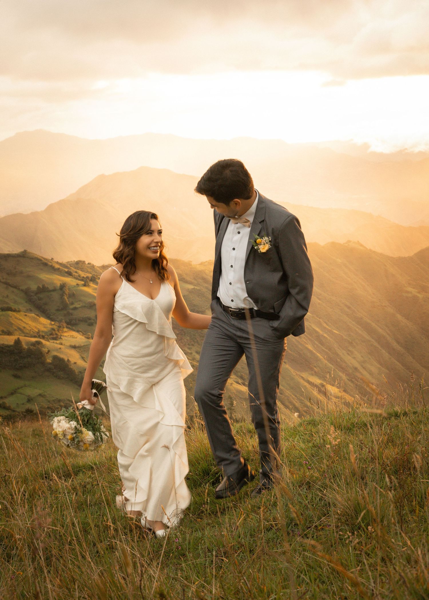 Newlyweds walk hand in hand through mountain wildflowers during a golden sunset in the mountains.