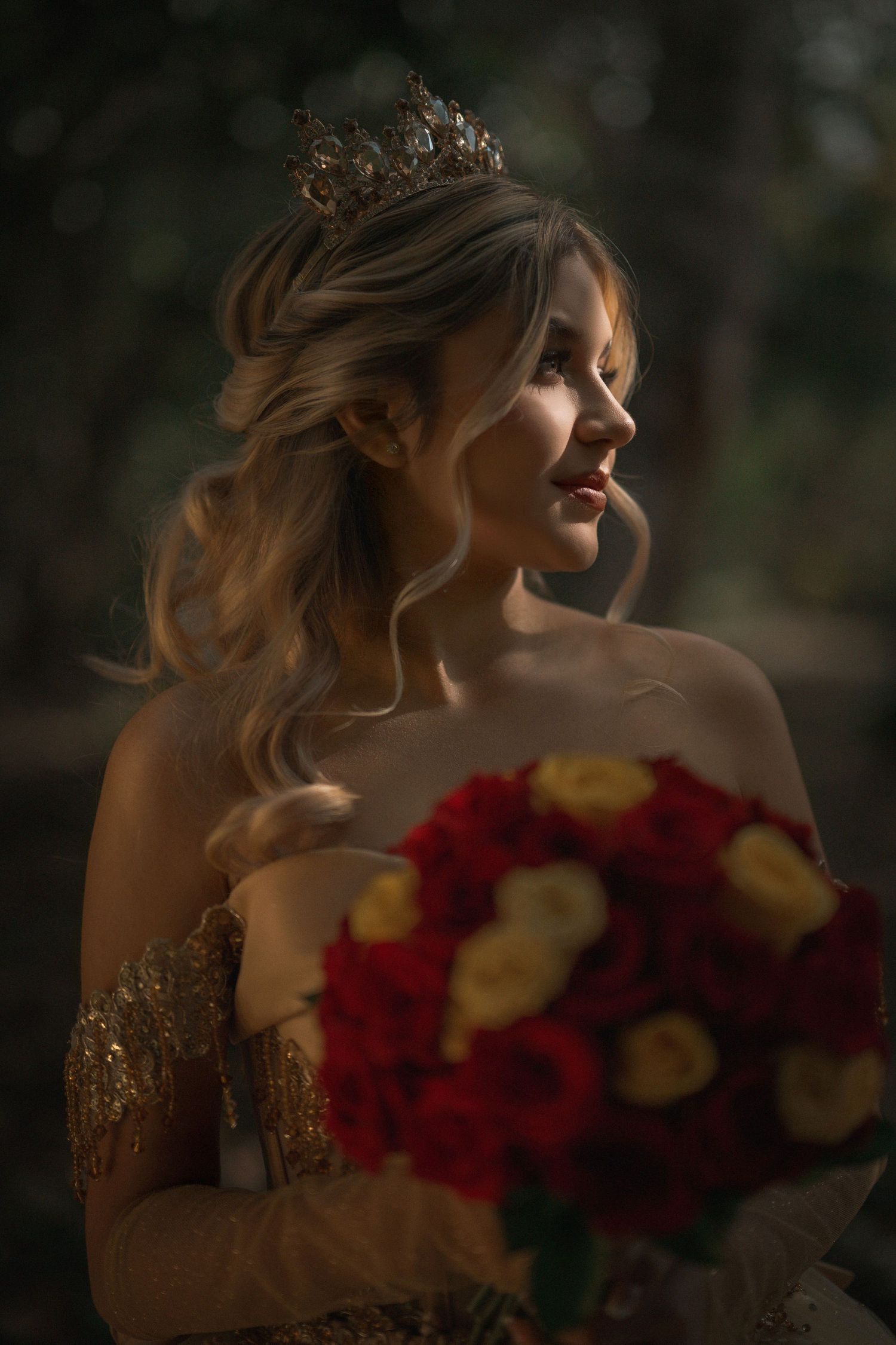 Artistic bridal portrait with red and yellow bouquet against moody dark background.
