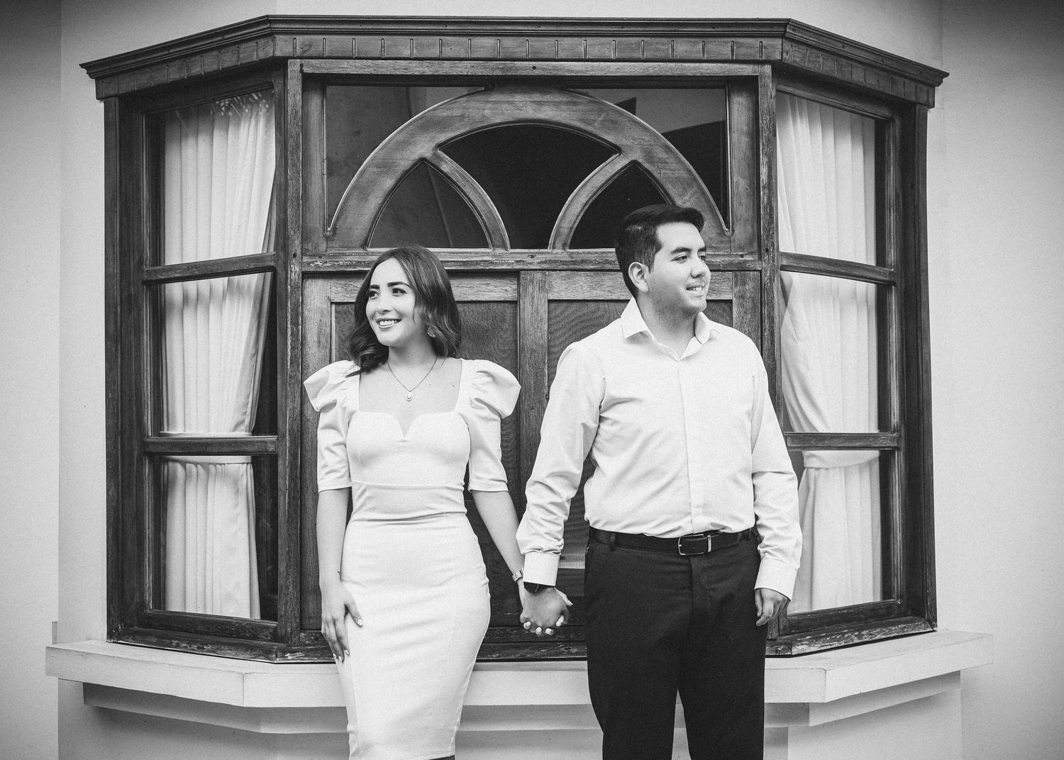 A series of black and white engagement photos showing a couple posing by vintage windows.