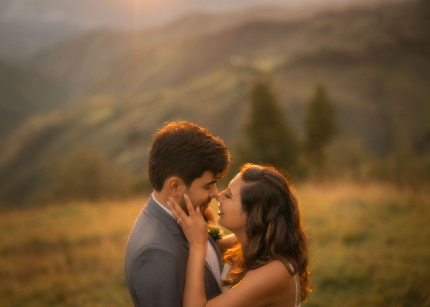 Romantic couple embraces during golden hour in a mountainous landscape at sunset.