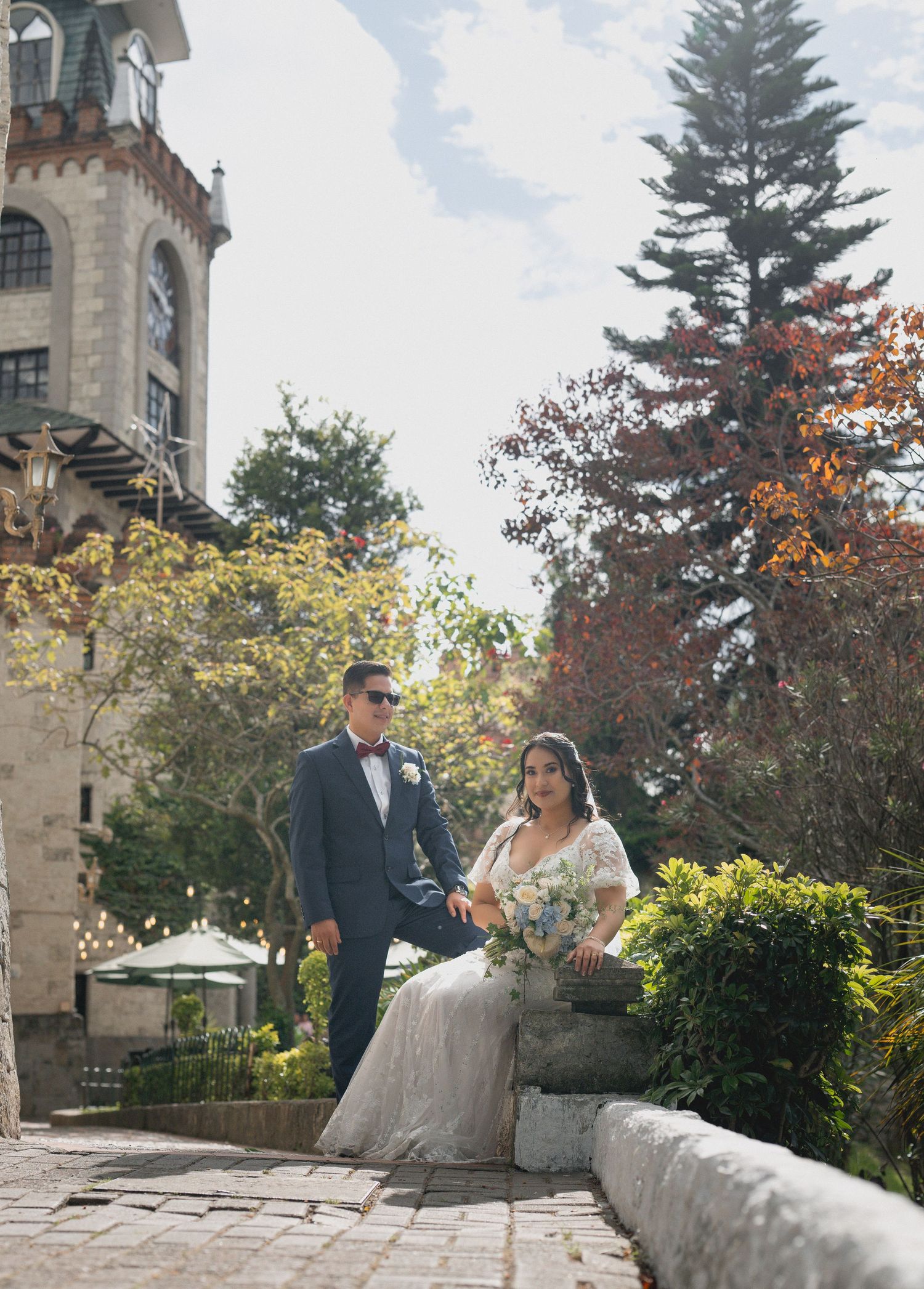 Newlywed couple poses together on stone steps surrounded by autumn foliage at an elegant outdoor venue.