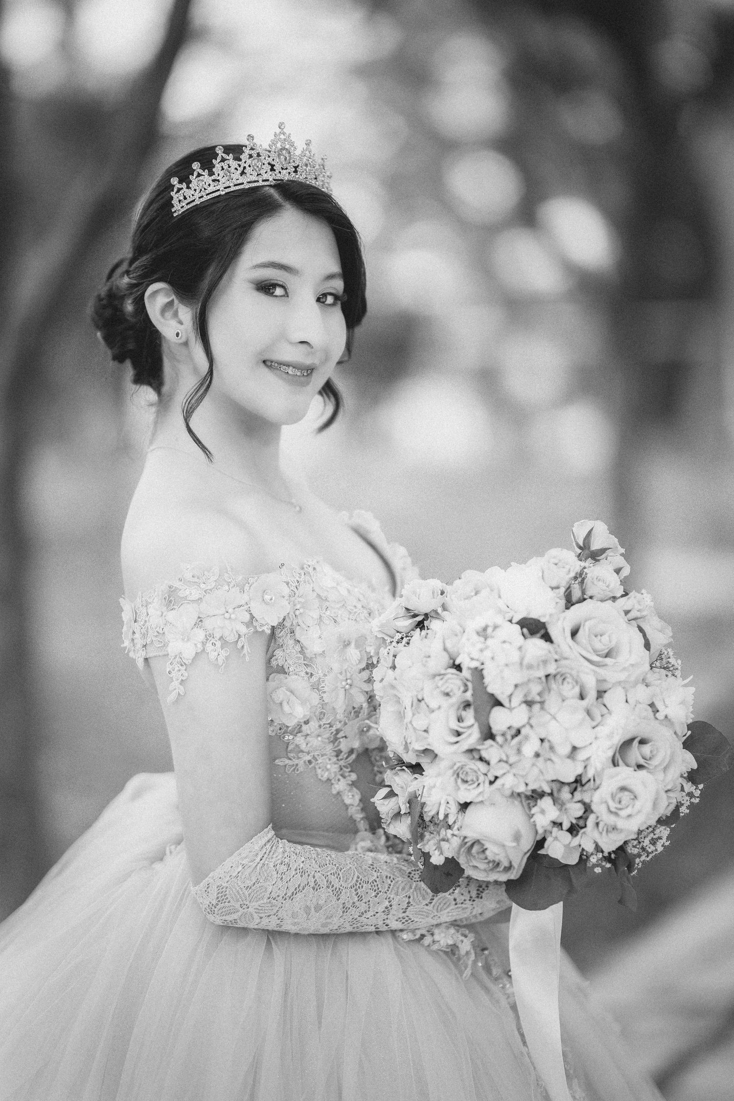 A bride in a white lace wedding gown holds an elegant bouquet of pink and white roses in a black and white photo series.