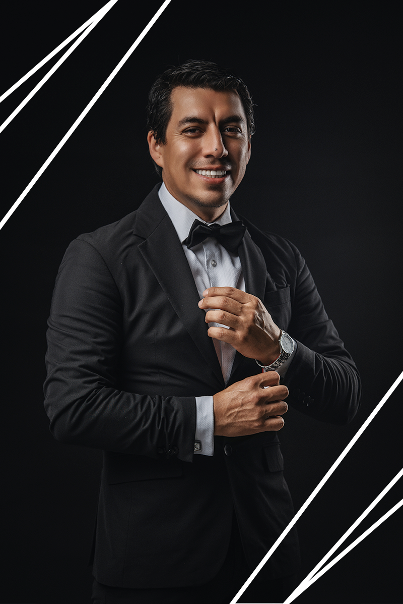 Professional portrait of someone in a black tuxedo and bowtie adjusting their cufflink against dark background with white lines.