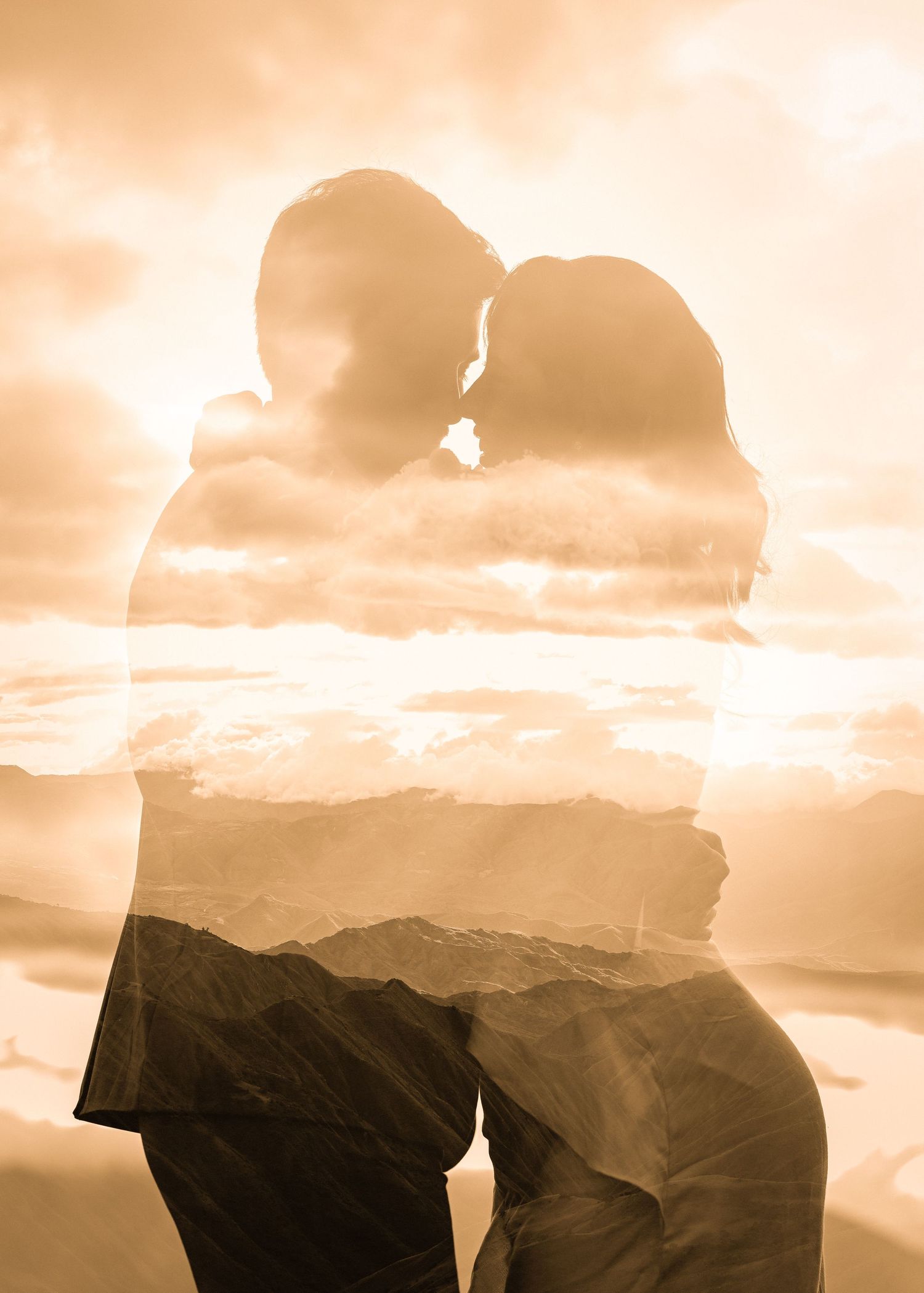 Silhouettes of a couple against a warm sunset sky with mountains in the background.