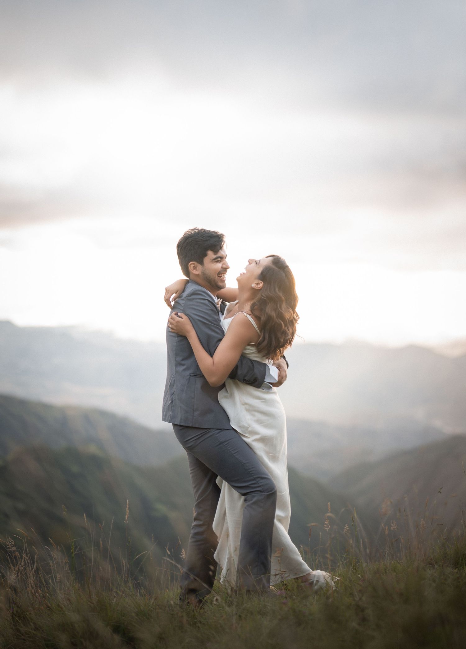 Wedding couple shares an intimate moment on a grassy mountainside with dramatic cloudy skies behind them.