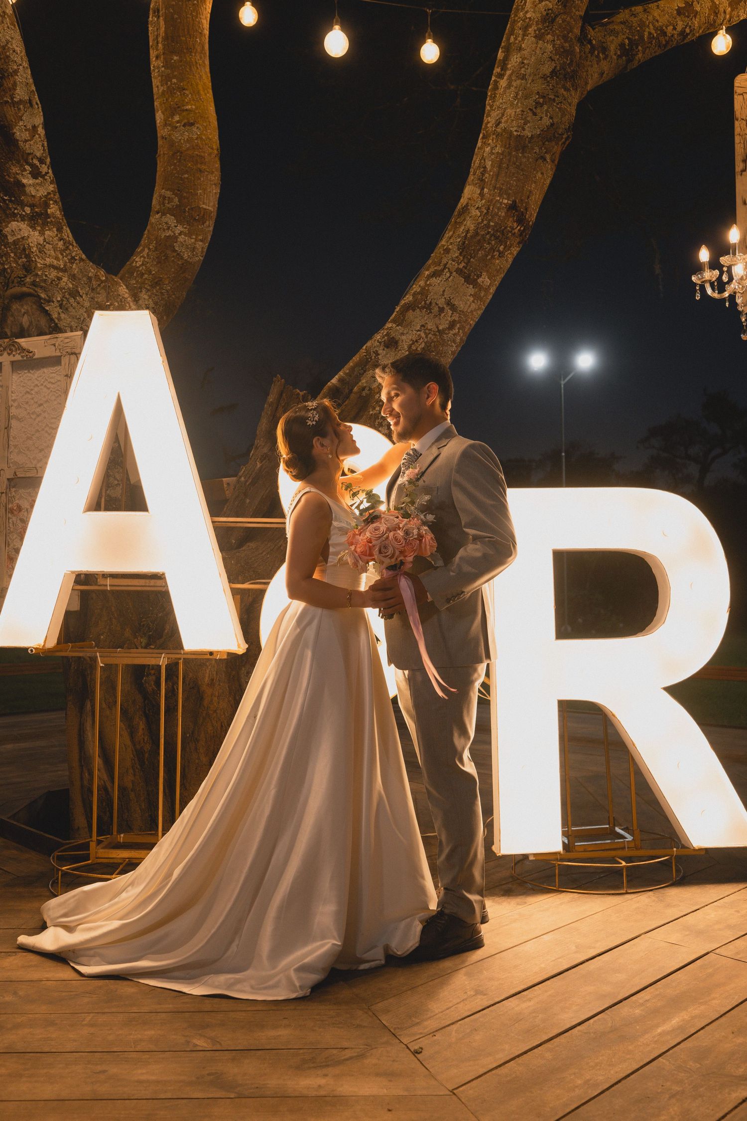 Romantic nighttime wedding photos with illuminated letters and string lights creating a magical atmosphere.
