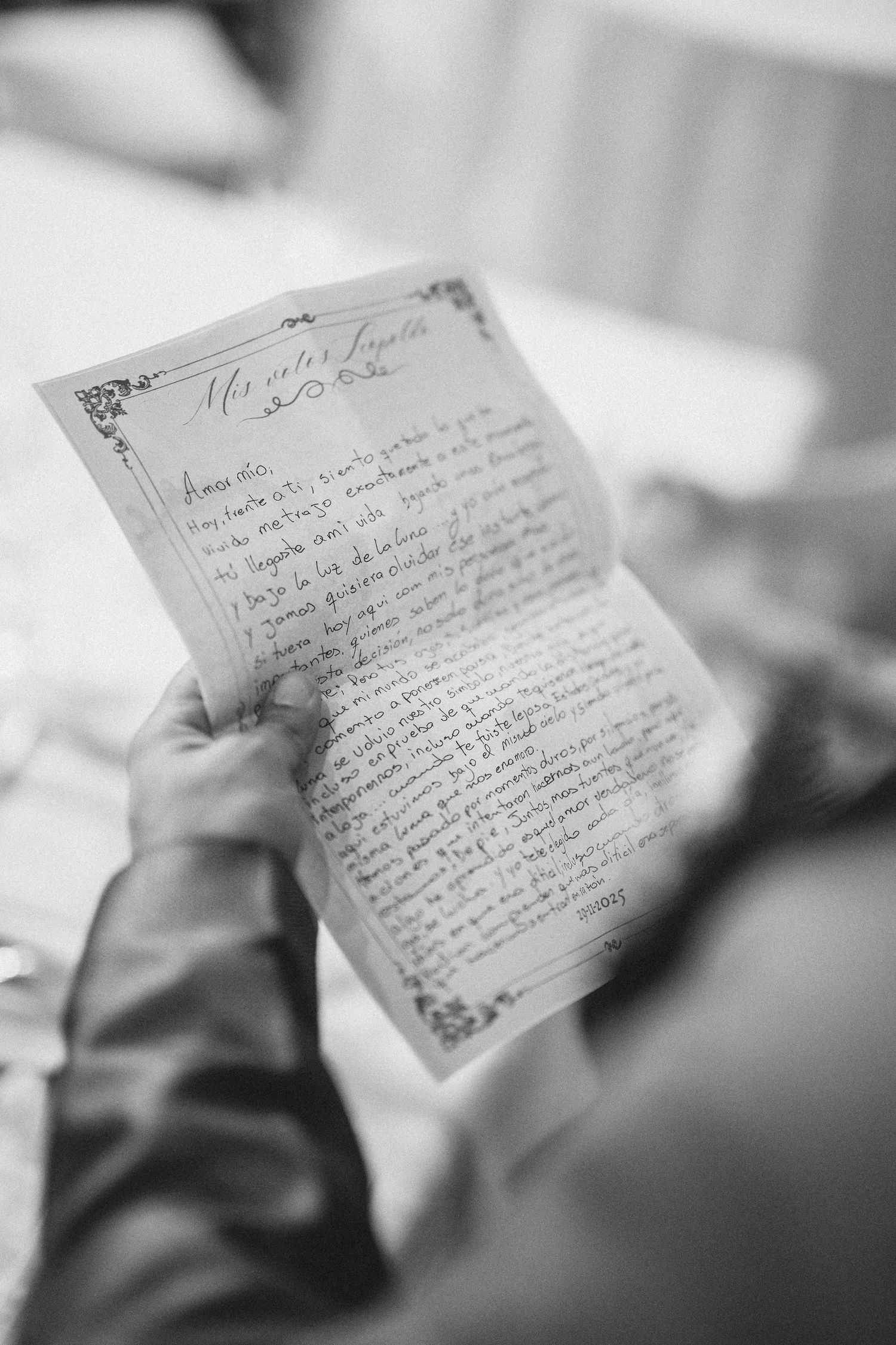 A handwritten letter with decorative border being held and read in black and white photography.