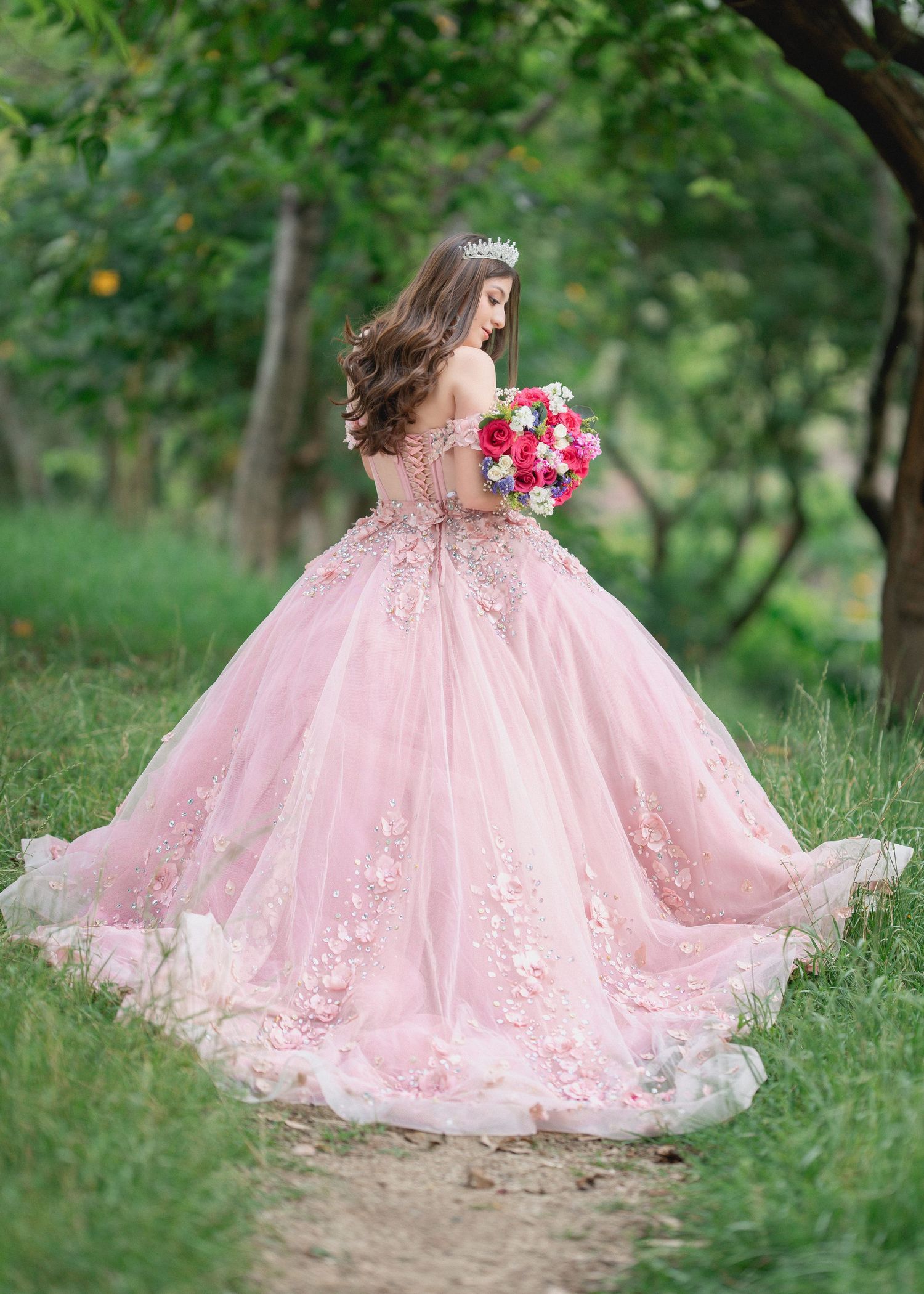A flowing pink ball gown with delicate floral lace details twirls gracefully in a lush green garden setting.