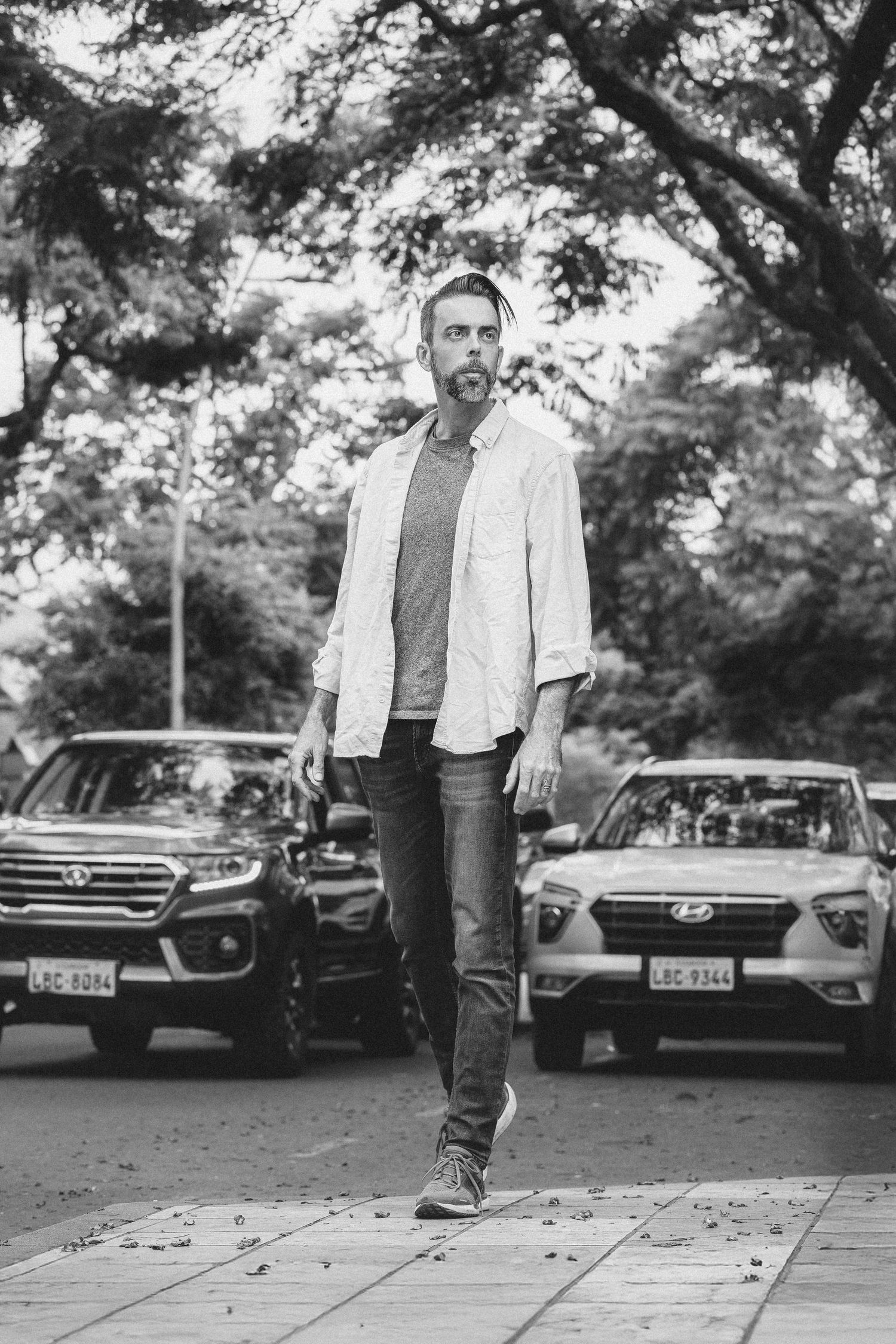 A sequence of four black and white photos showing someone walking along a sidewalk with parked cars in the background.