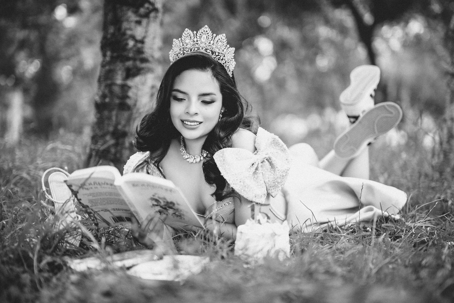 A dreamy black and white photo series shows someone in a white dress and tiara lying gracefully in a garden setting.