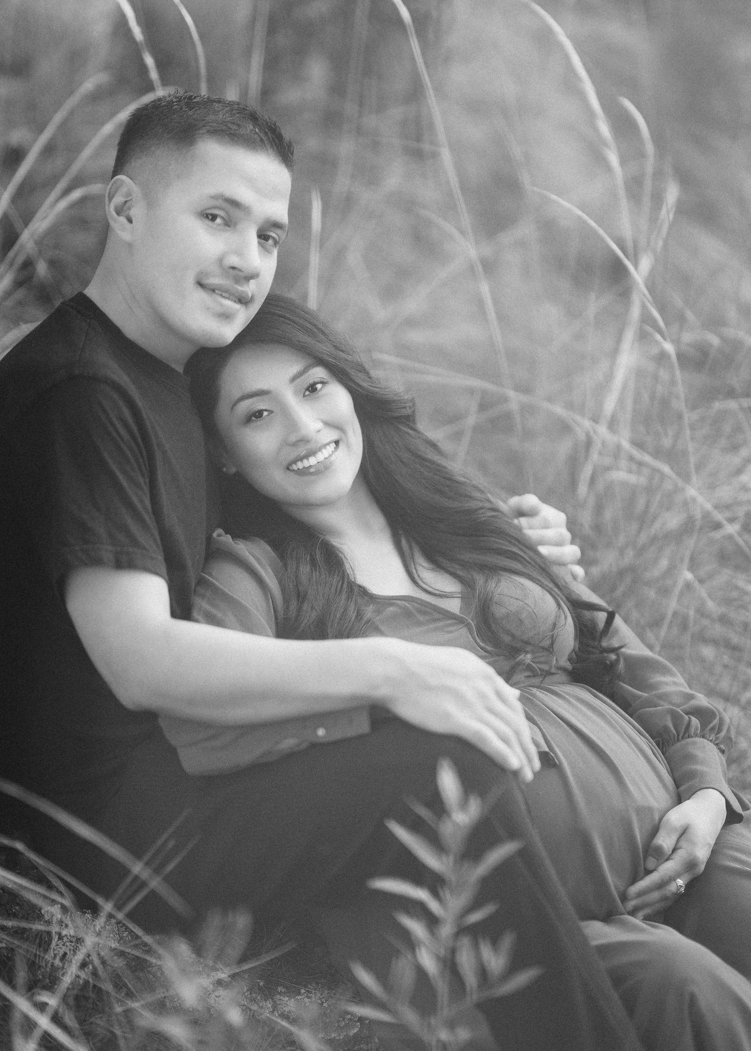 A couple lies together in tall grass during a romantic black and white outdoor photoshoot.