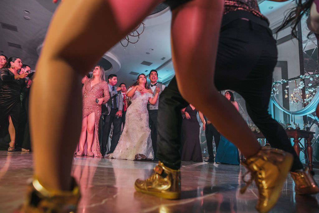 People dancing at a celebration with gold shoes visible in the foreground and a crowd in the background.