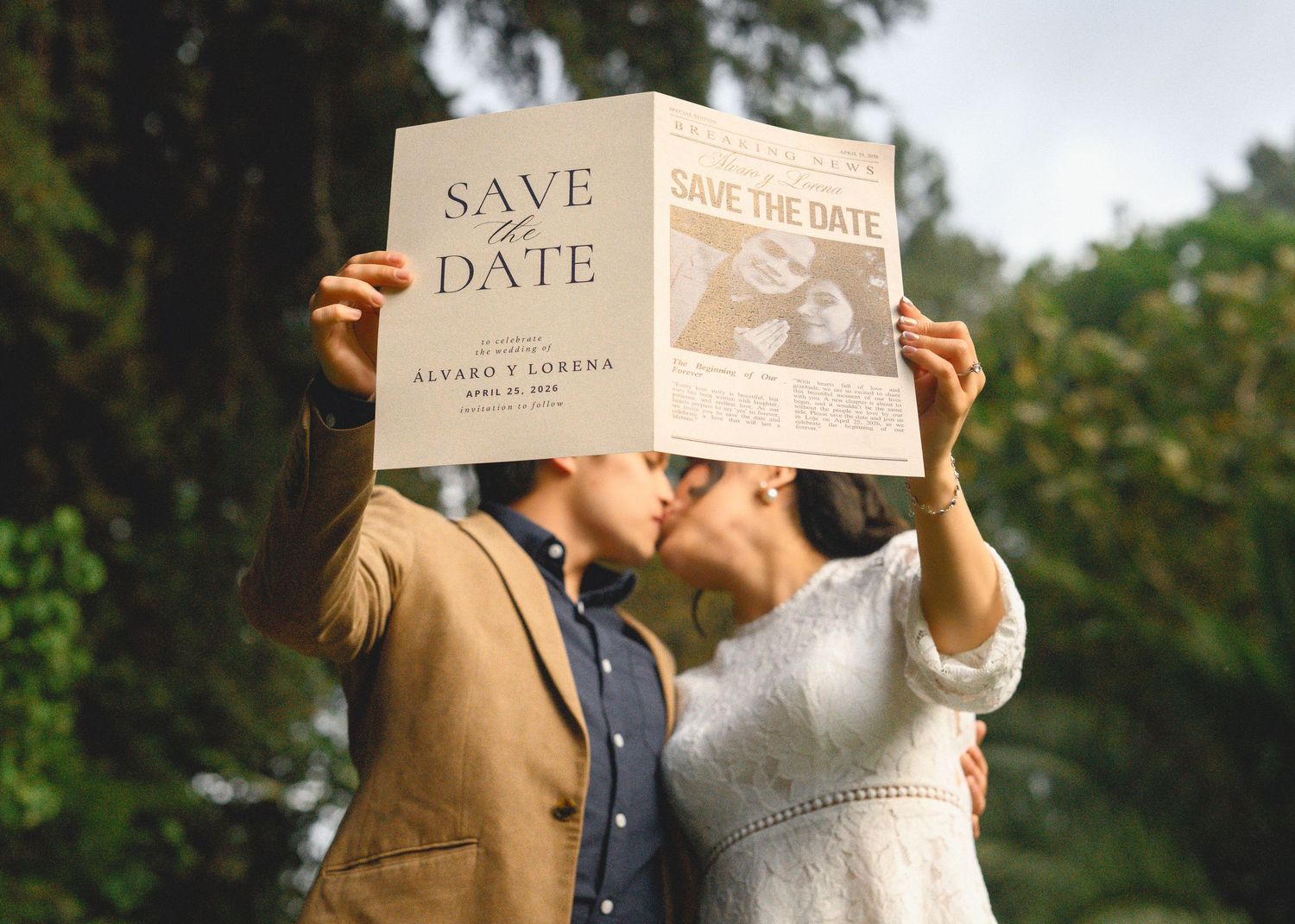 A couple holding up save the date wedding announcement cards in an outdoor garden setting.