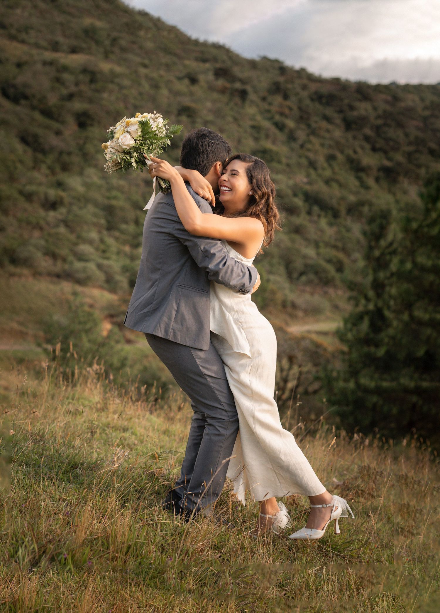A couple embraces and dances together on a grassy hillside during a romantic moment.