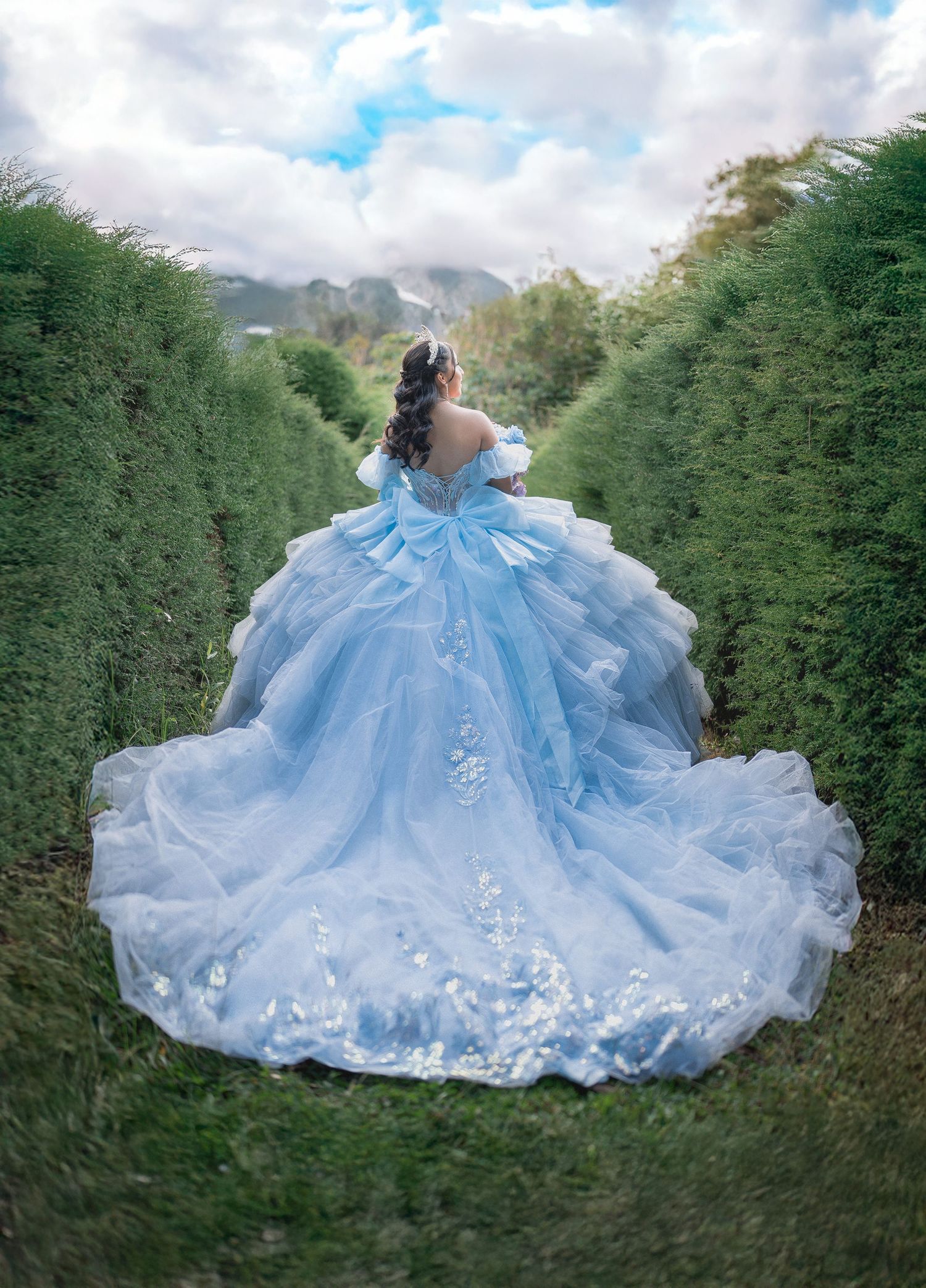 A flowing light blue ballgown dress spreads across lush green grass in a dreamy outdoor garden setting.