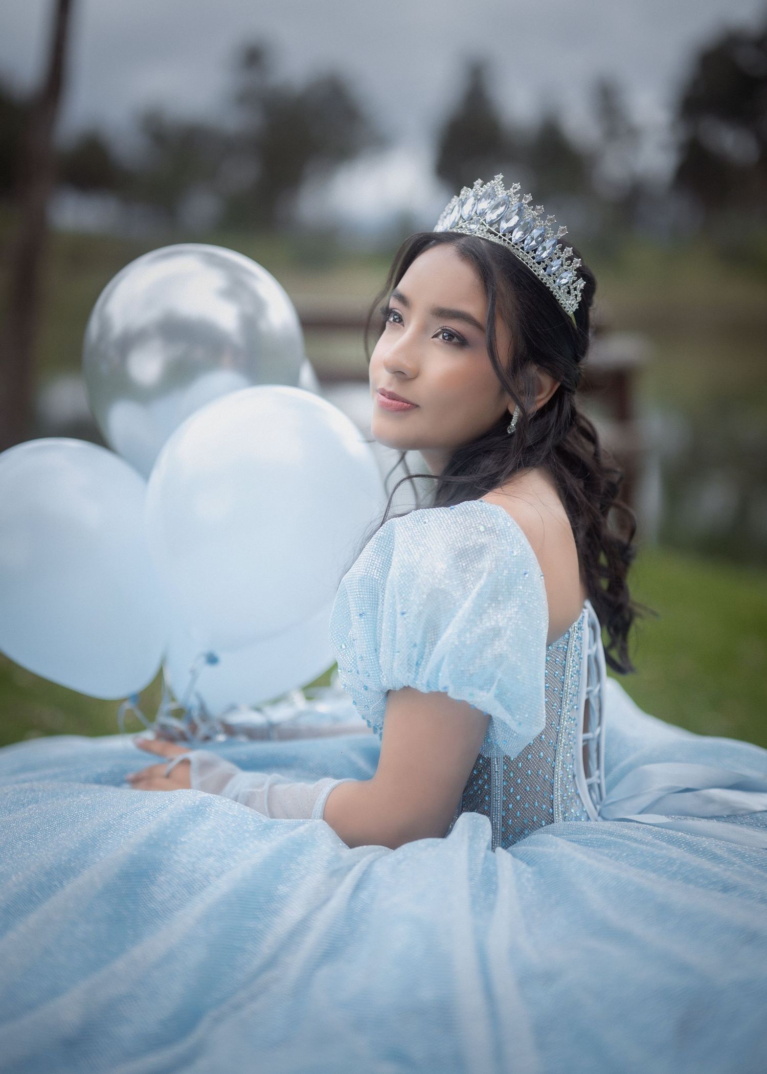 A quinceañera photo session featuring a young woman in a light blue ball gown posing gracefully in an outdoor setting.