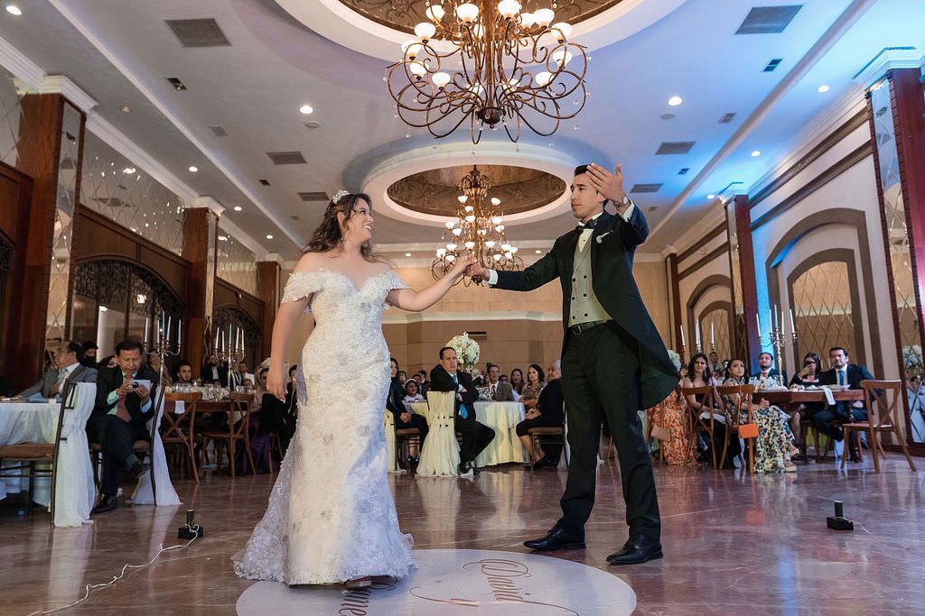 Couple performs their first dance in an elegant ballroom with crystal chandeliers and ornate decor.