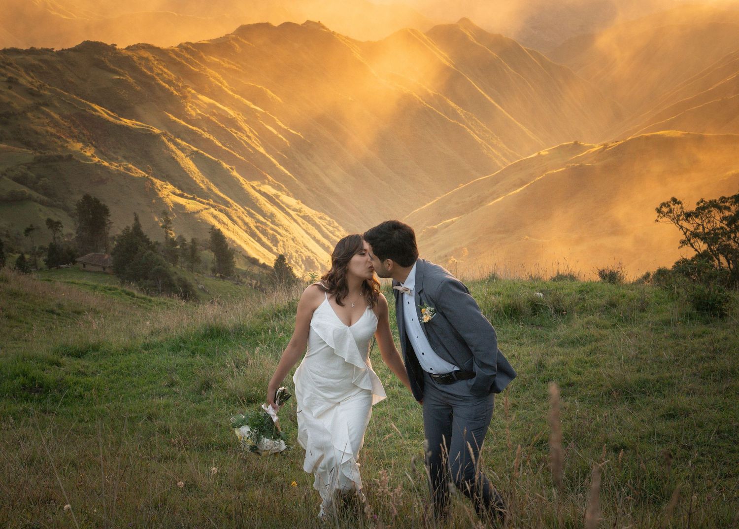A couple shares a romantic moment during golden hour in a mountainous landscape with dramatic sunlight streaming through clouds.