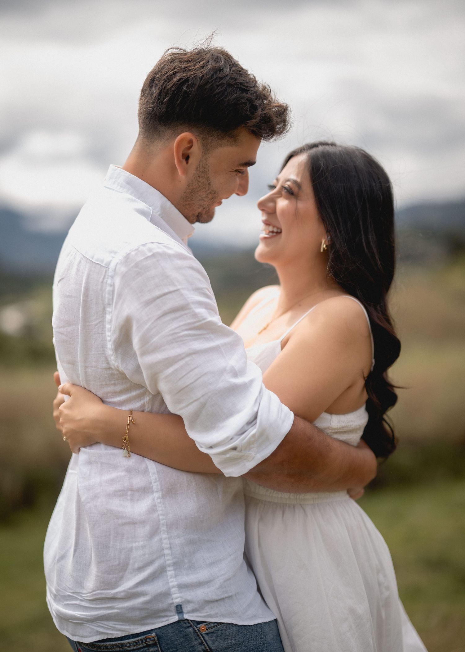 A couple in white attire share an intimate embrace while dancing outdoors in a romantic moment.