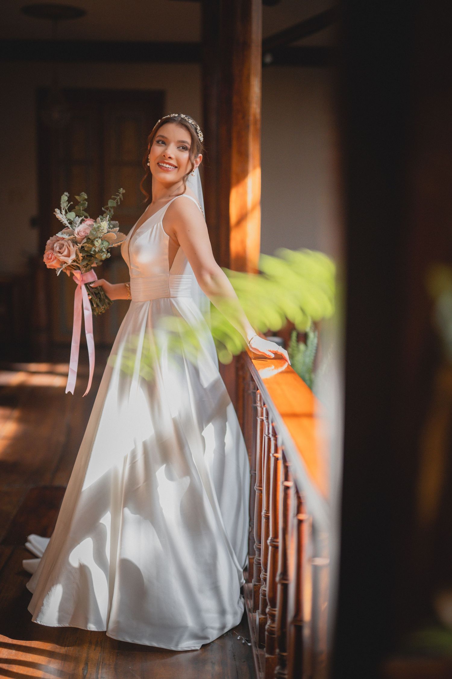 An elegant white wedding gown photographed in warm sunlight against wooden interior details.