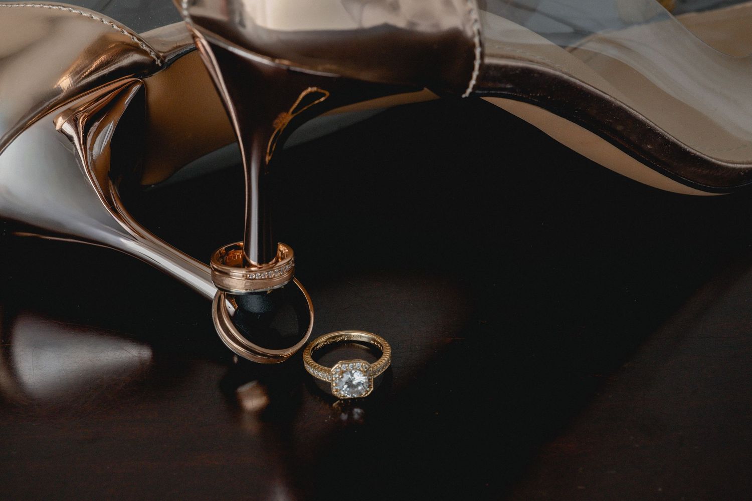 Close-up view of golden wedding rings with diamonds resting on a dark wooden surface in warm lighting.