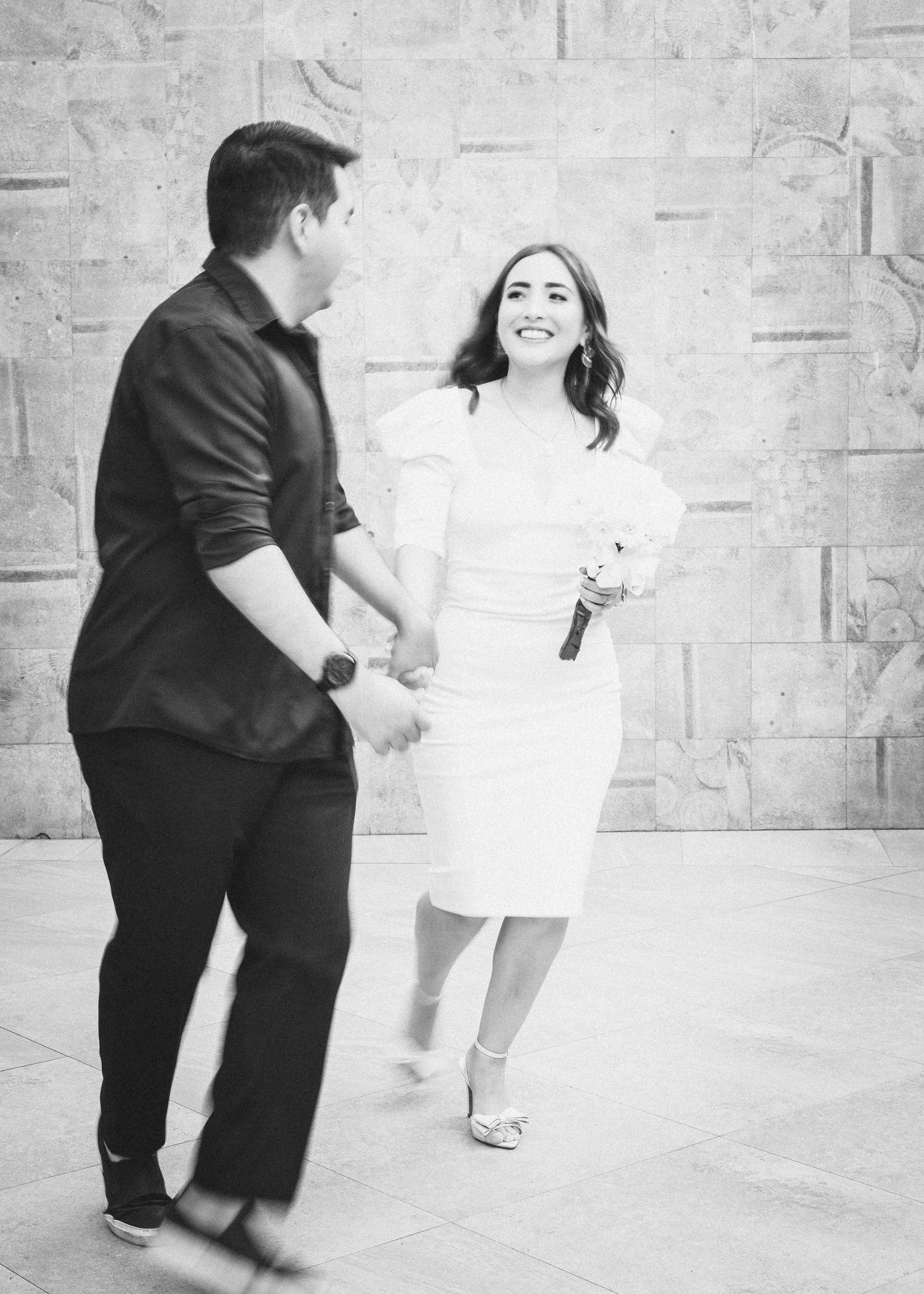 A series of black and white photos showing two people dancing together in a joyful sequence against a light wall.