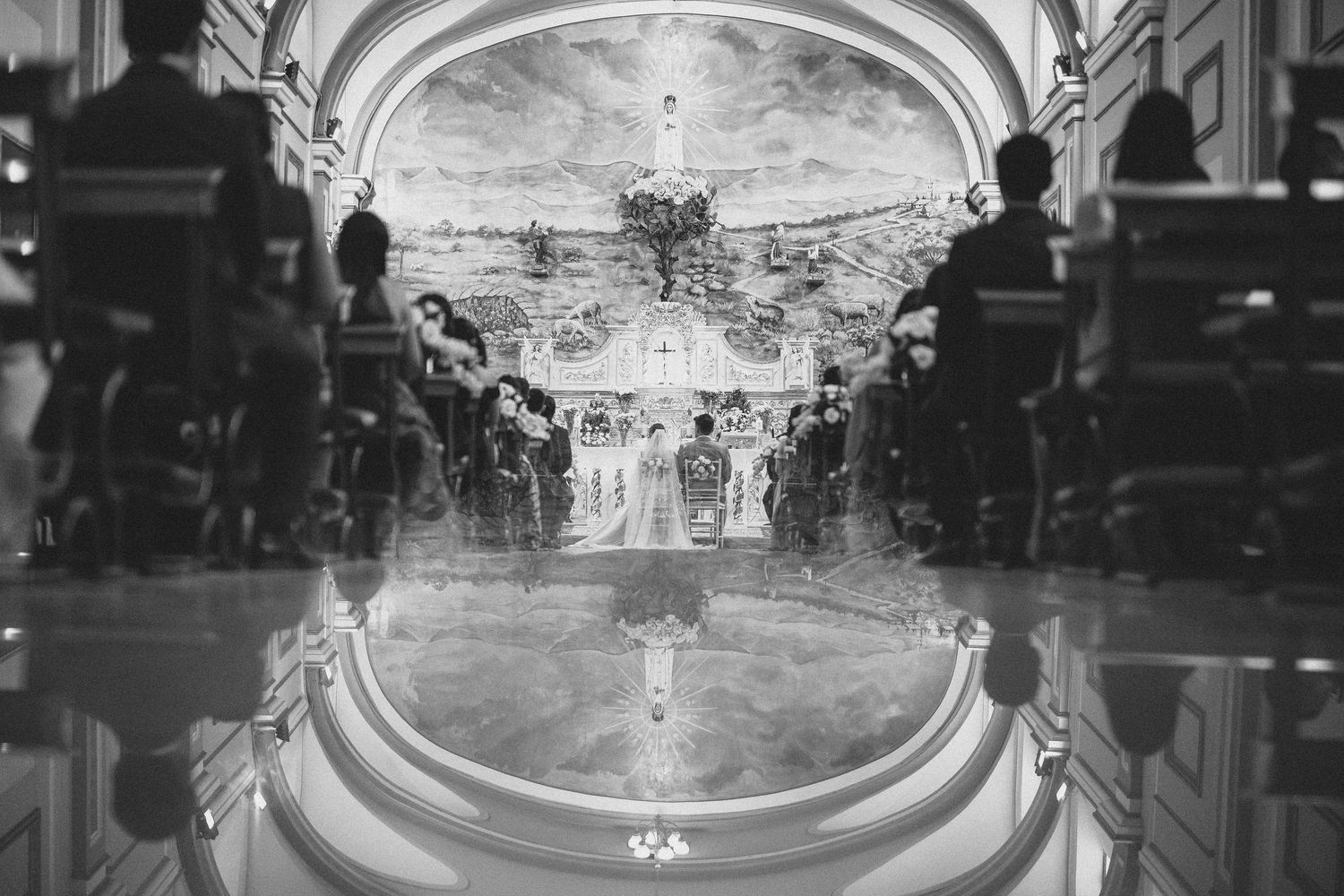 Black and white wedding ceremony in an ornate church with dramatic mirror reflection on the floor.