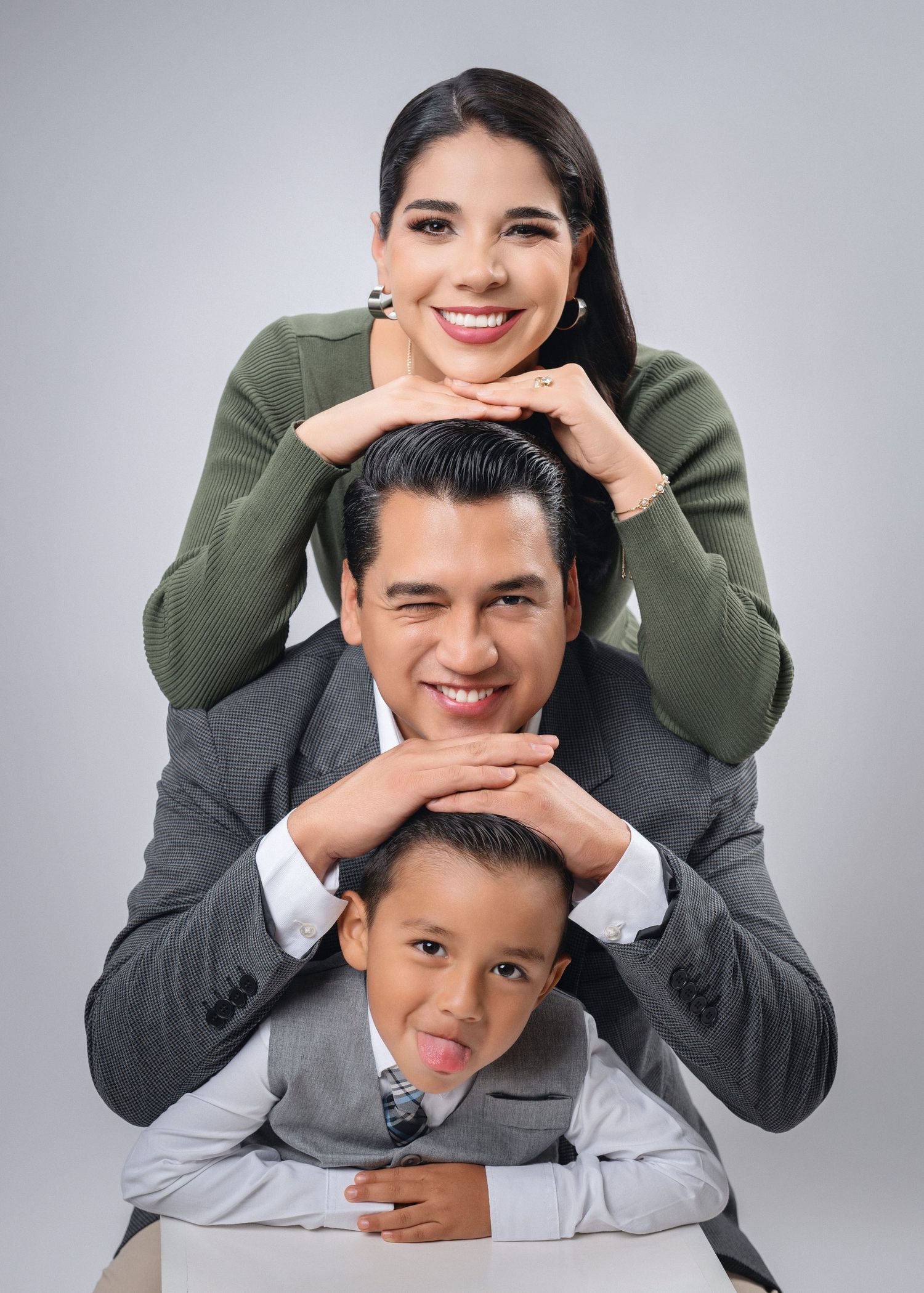 Three people pose together in a stacked formation wearing olive green and grey outfits against a light background.