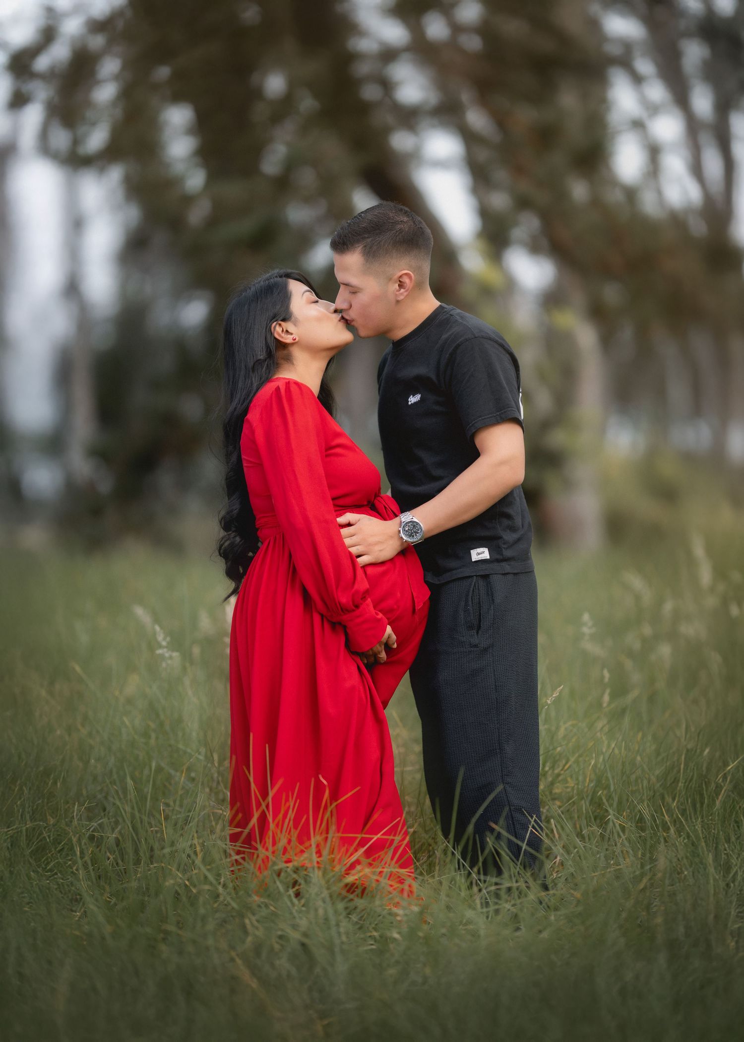A romantic couple embraces in a grassy field, with the woman wearing a vibrant red dress.