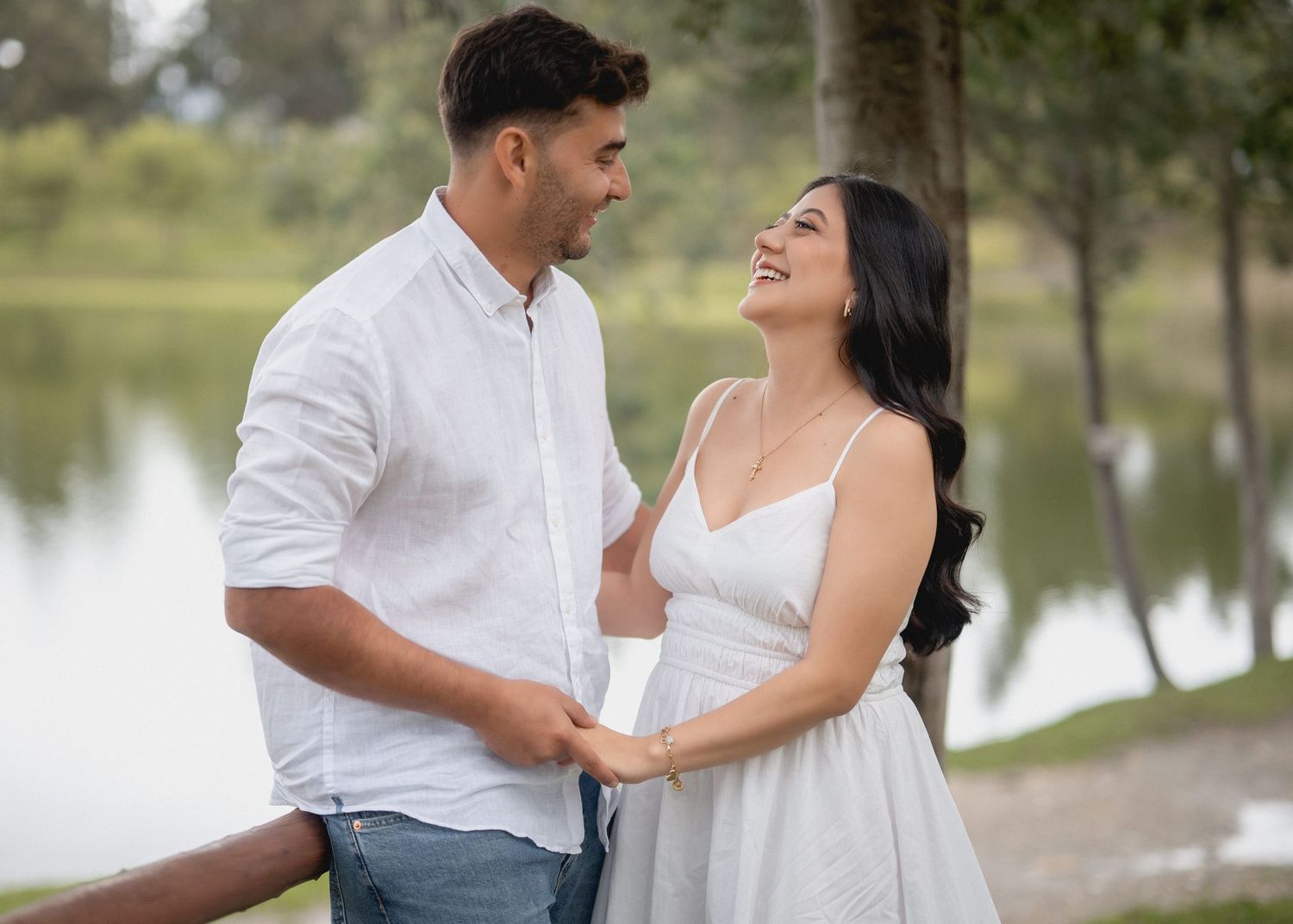 A couple in white attire shares romantic moments by a lakeside during a photo session.