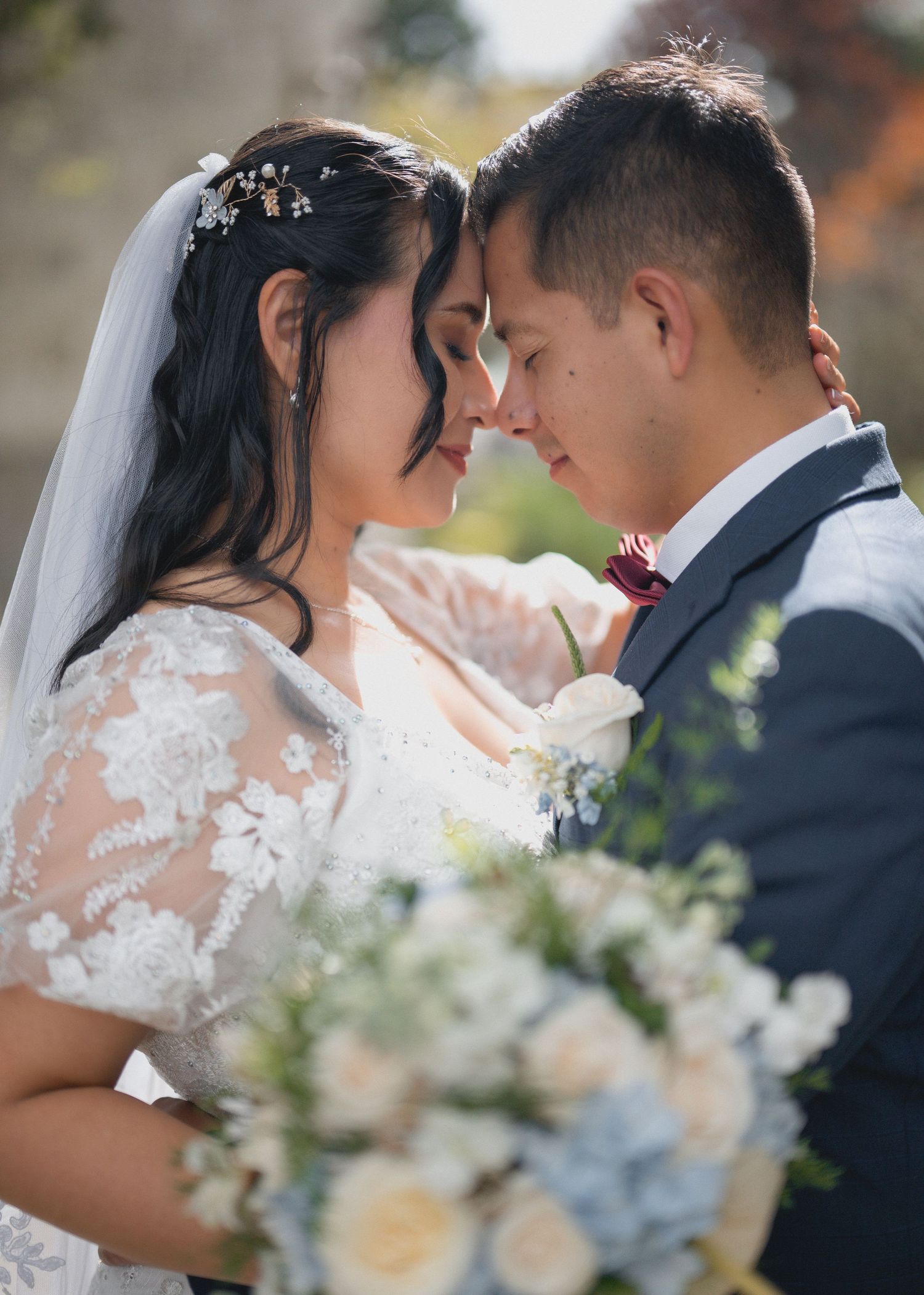 A romantic wedding portrait showing a couple in traditional attire with a soft-focused floral bouquet in the foreground.