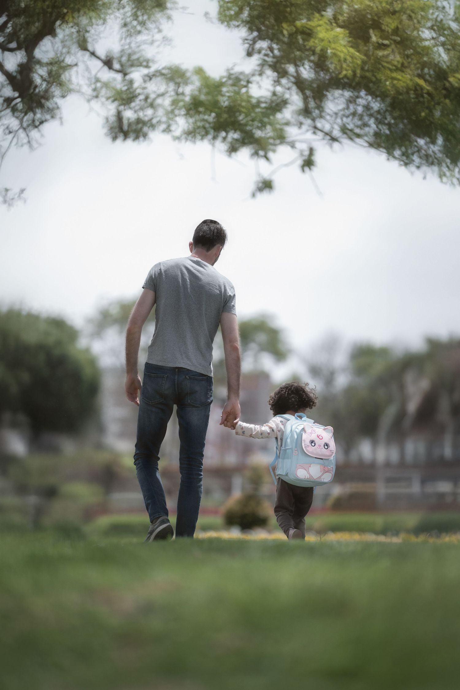 A parent and small child walk hand in hand across a grassy field on a misty day.