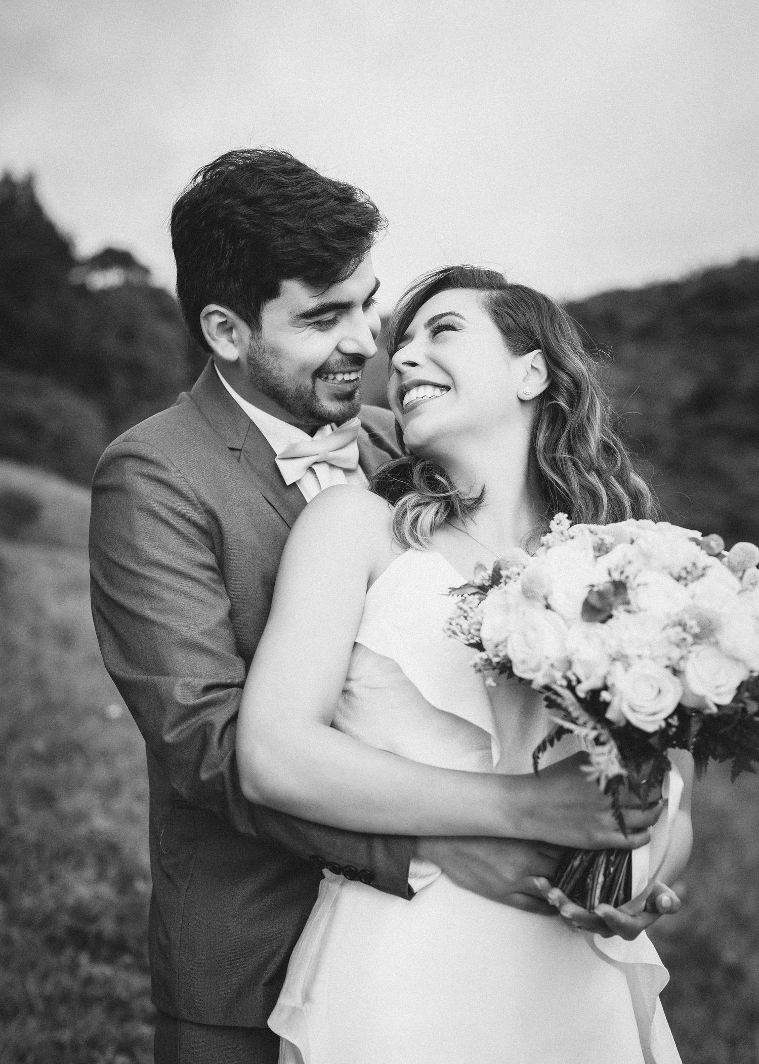 A romantic black and white wedding photo series showing a couple laughing and embracing in an outdoor setting with a bouquet.