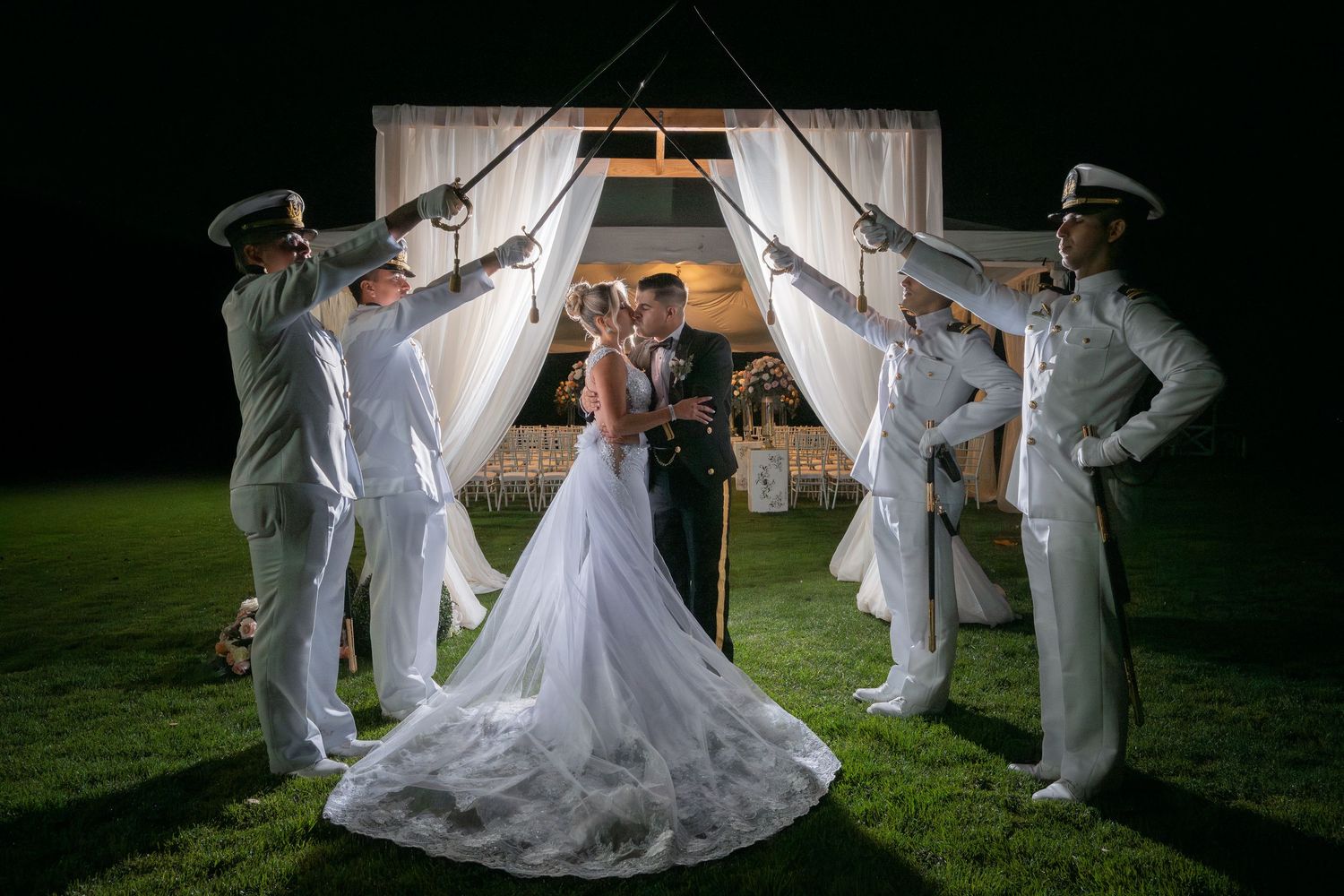 Wedding party members in light gray suits create dramatic poses with flowing white dress fabric at night.