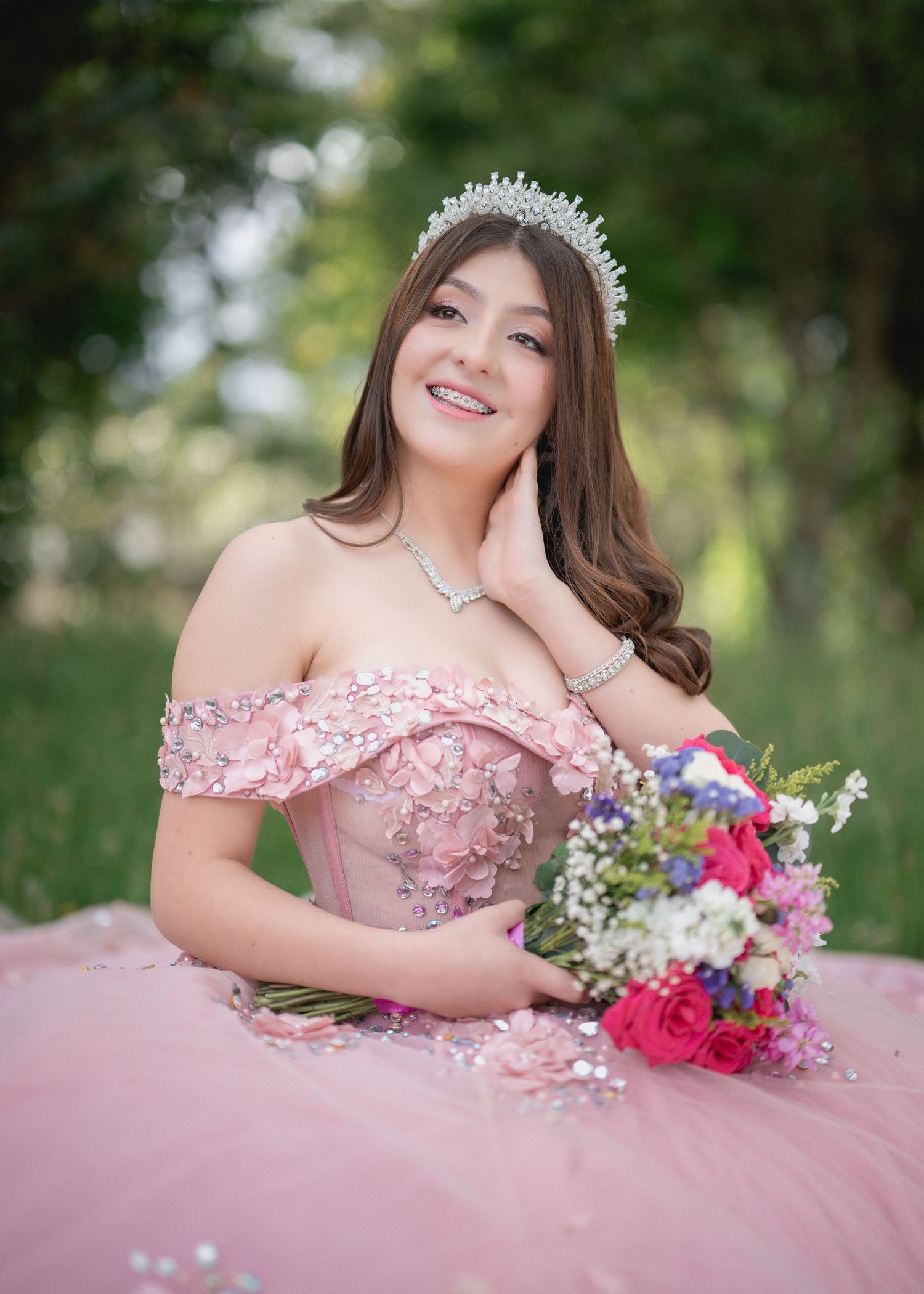 A person in a pink off-shoulder ball gown poses outdoors with a vibrant floral bouquet.