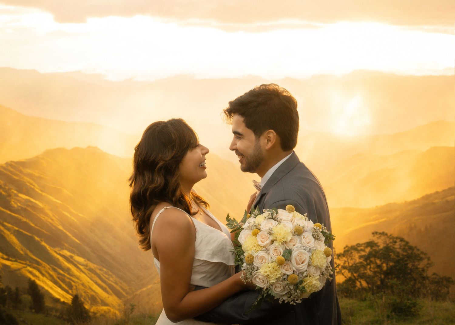 A couple embraces during golden hour on a mountaintop with a bouquet of white flowers and dramatic sunset views.