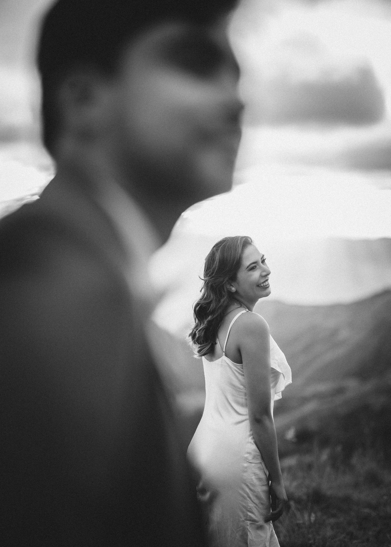 A black and white artistic wedding portrait shows a bride in profile with blurred figures in the background.