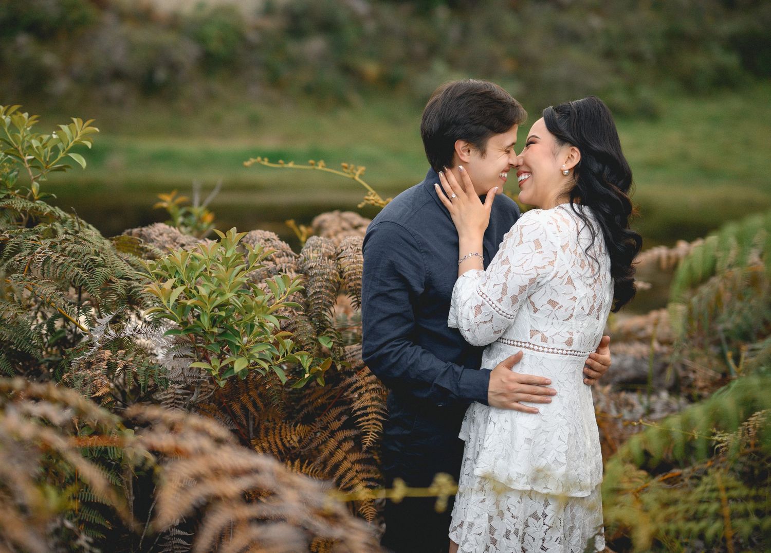 A romantic couple embraces in a lush garden setting during an outdoor photoshoot.