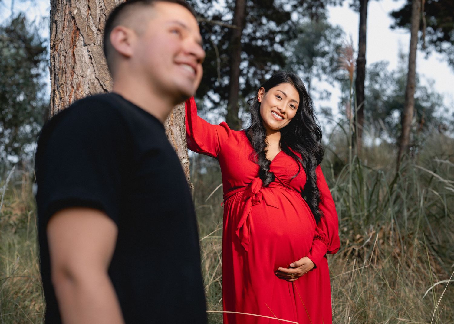 A couple in casual attire shares a joyful moment together during an outdoor photoshoot in a wooded setting.
