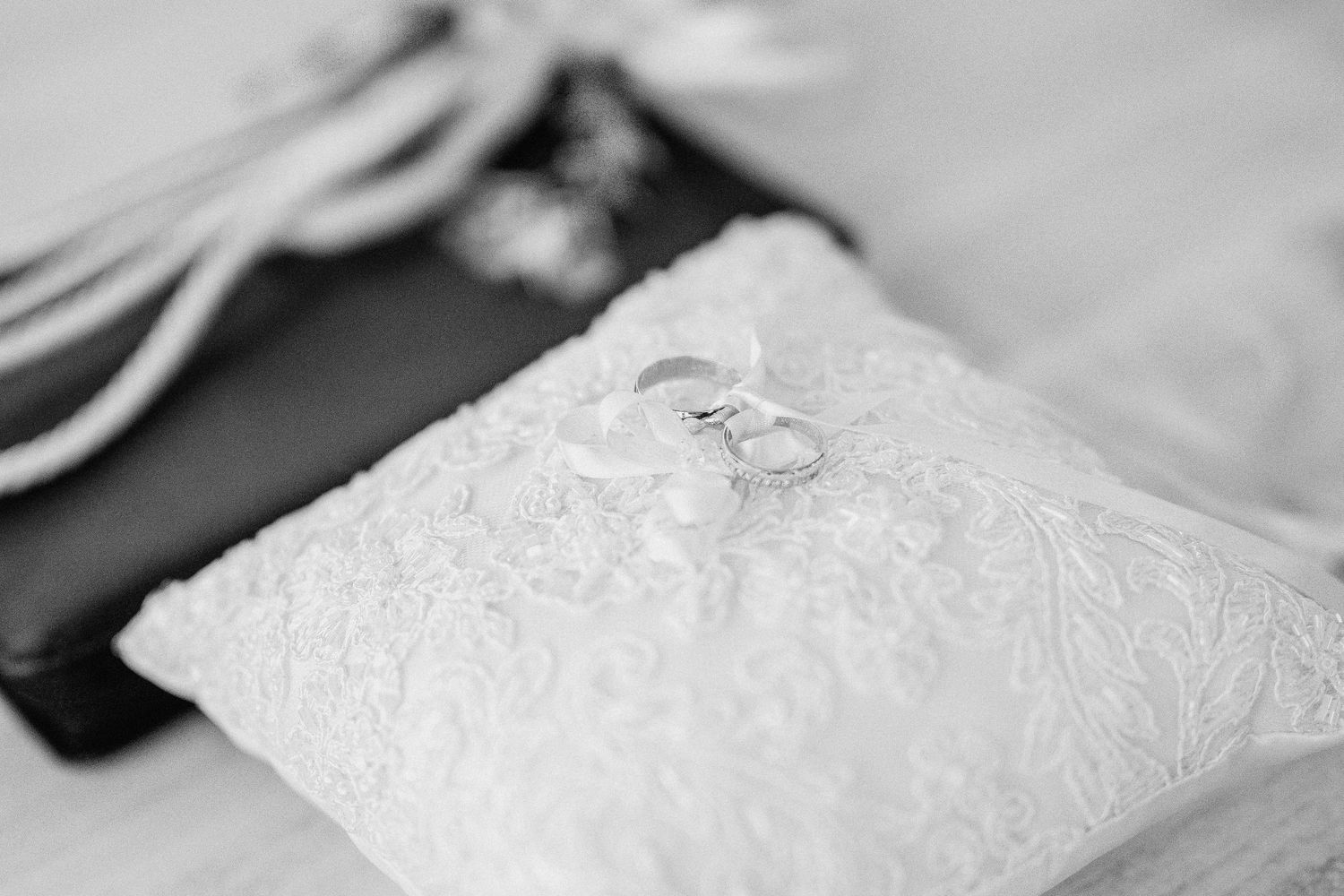 A delicate white lace wedding dress hangs on display against a light background.