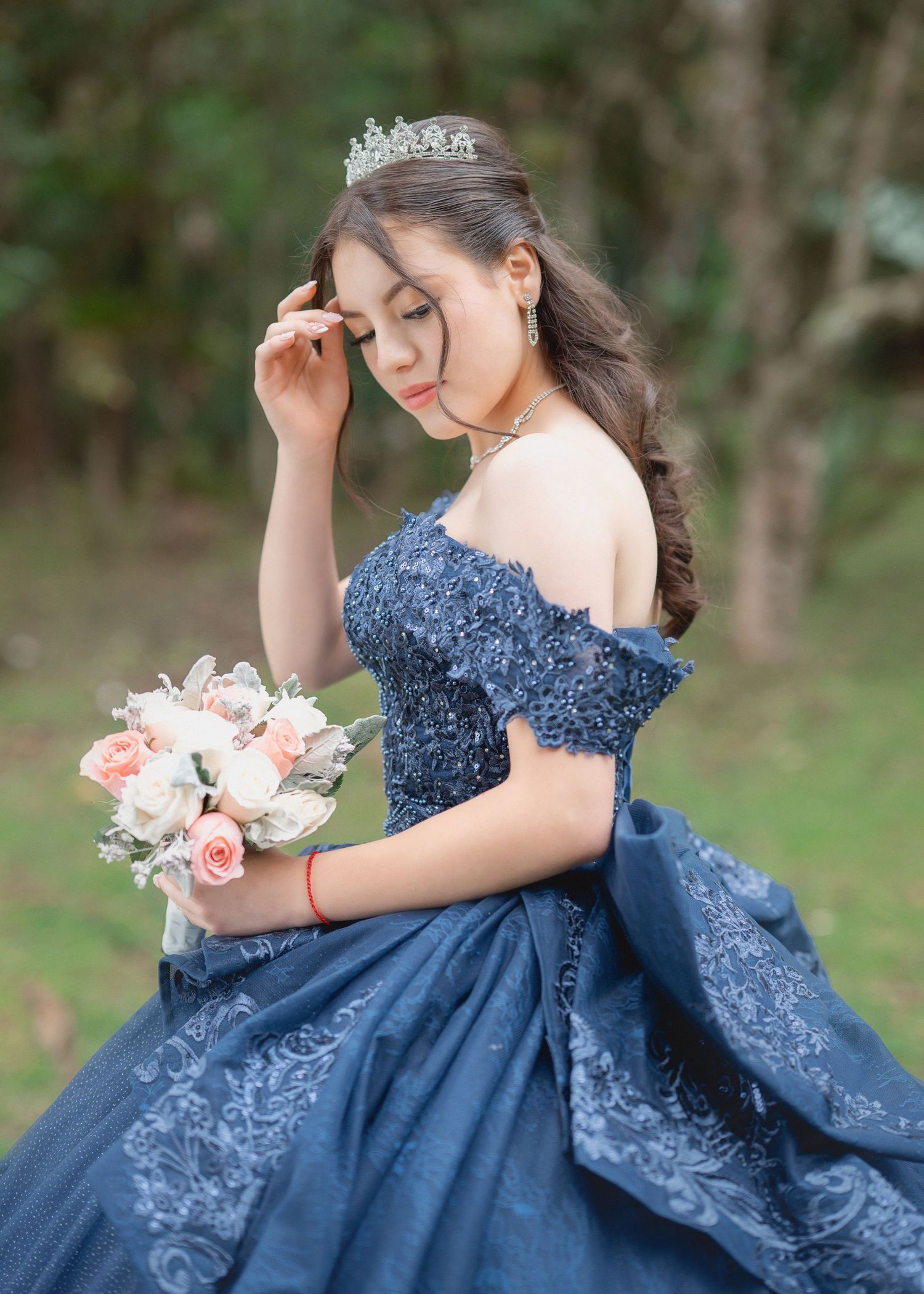 A person in an elegant navy blue embellished gown poses gracefully in a garden setting with a floral bouquet.