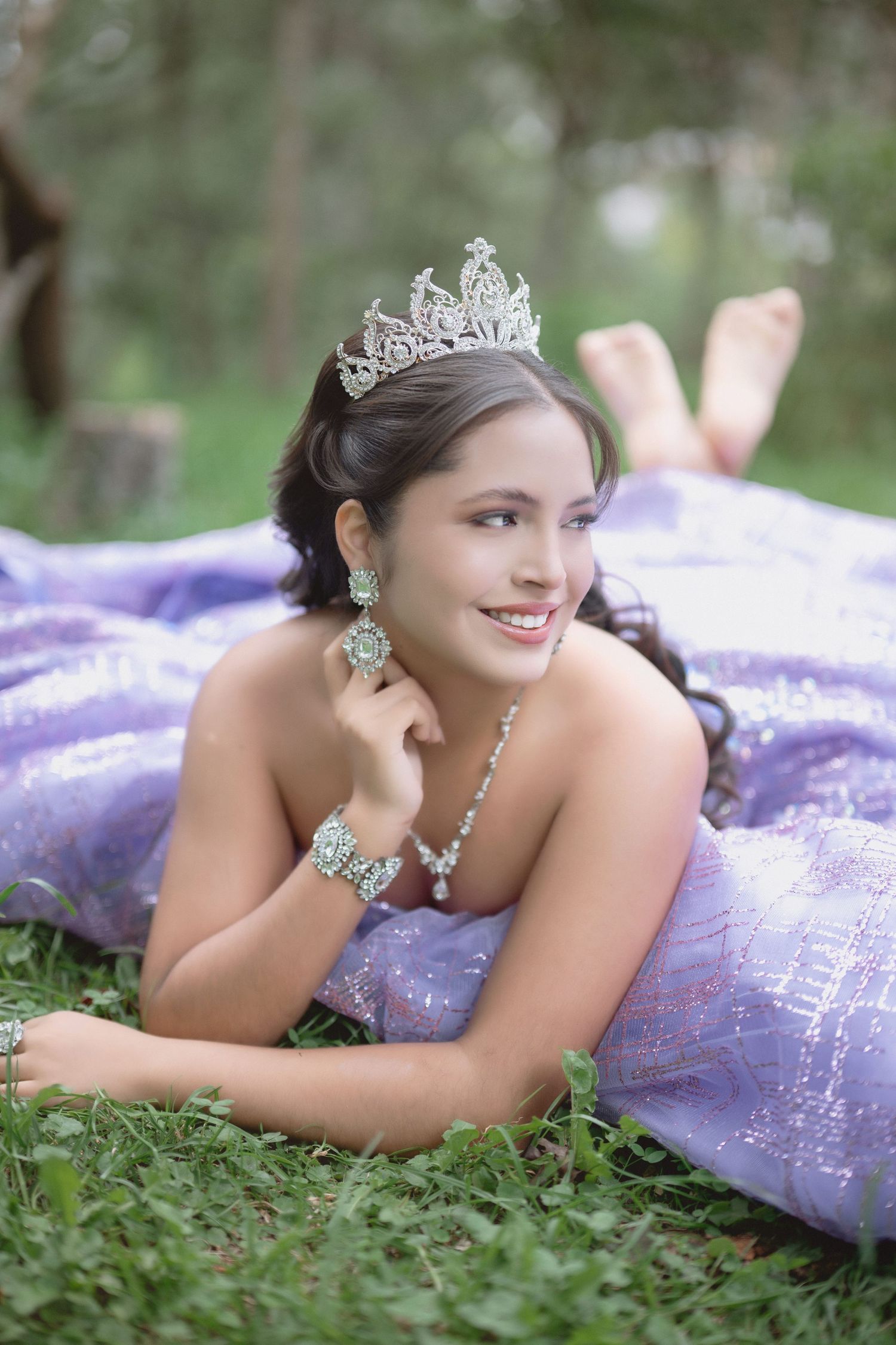 A person in a purple gown and tiara lies on grass in an outdoor photo session.
