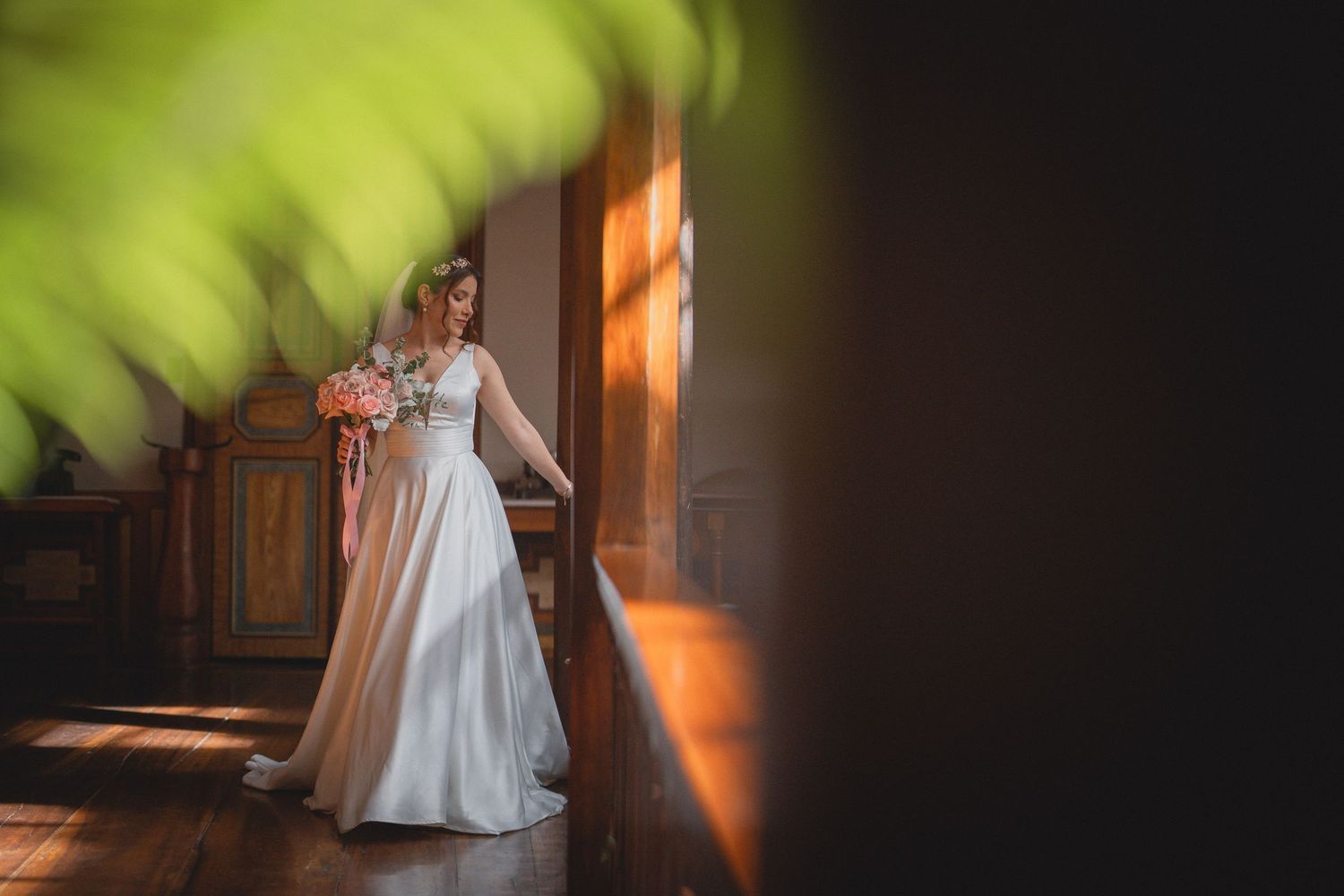 A bride in a white wedding dress stands in a warmly lit hallway creating an elegant silhouette.
