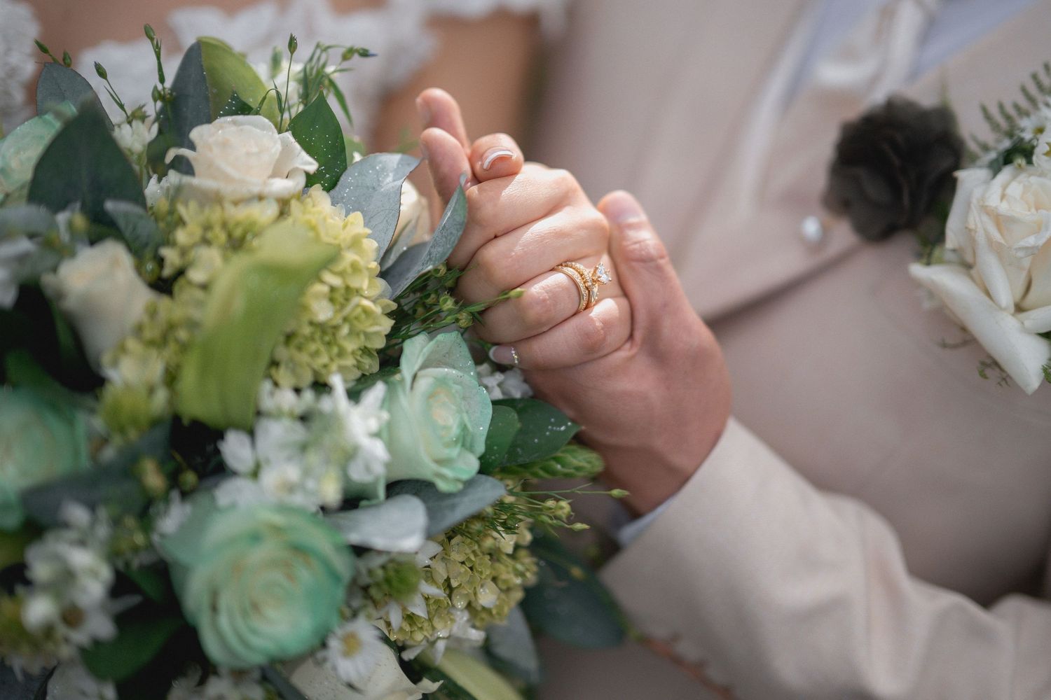 Delicate white and green floral bouquet with roses and greenery held against a light background.