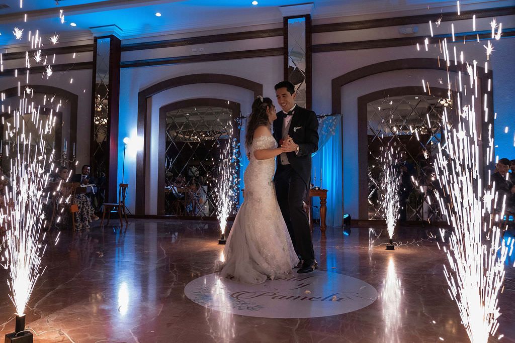 Indoor wedding reception with cold spark fireworks creating dramatic sparkler effects along a dance floor in blue lighting.