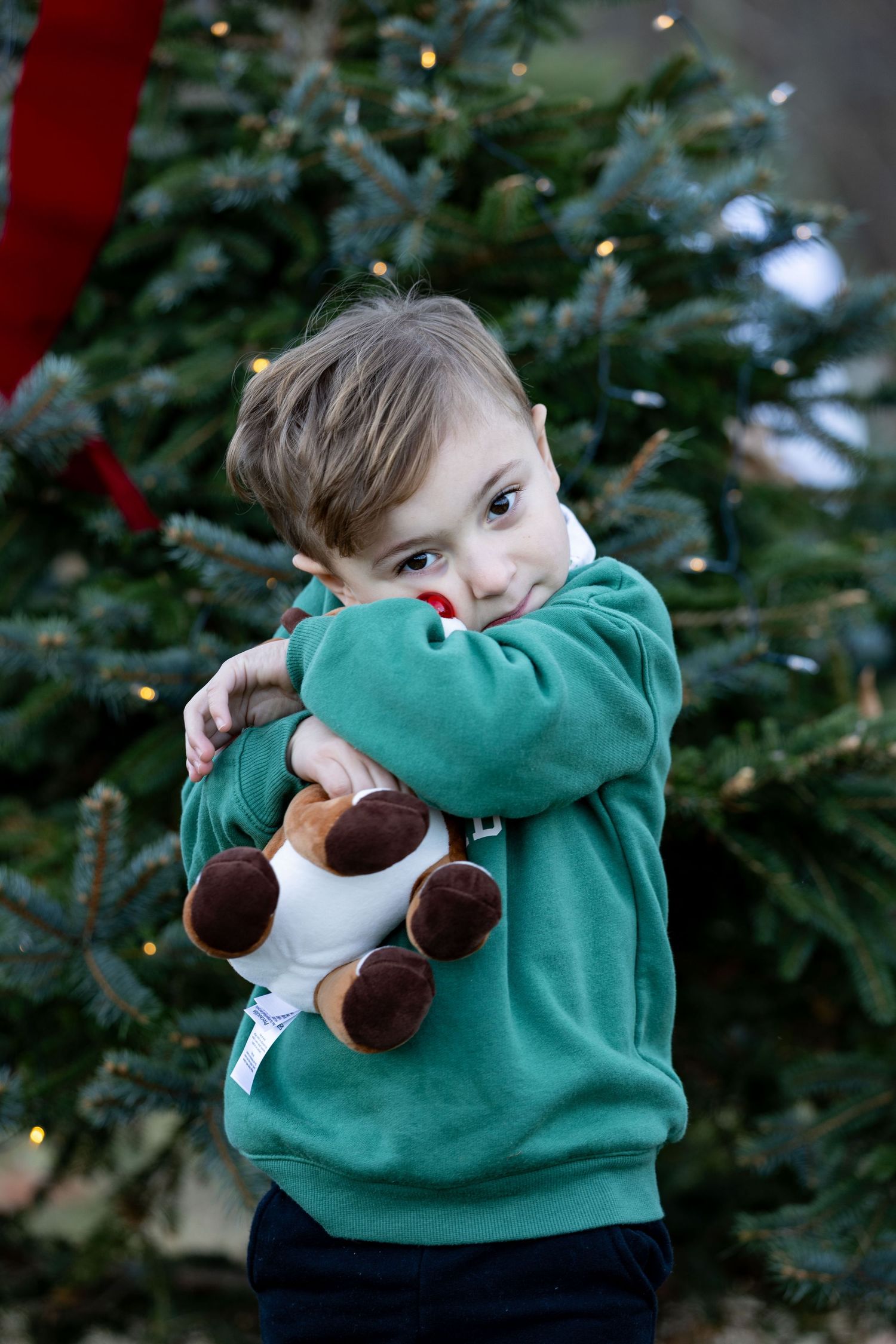 Child in green sweater playing with plush snowman toy during holiday photoshoot.