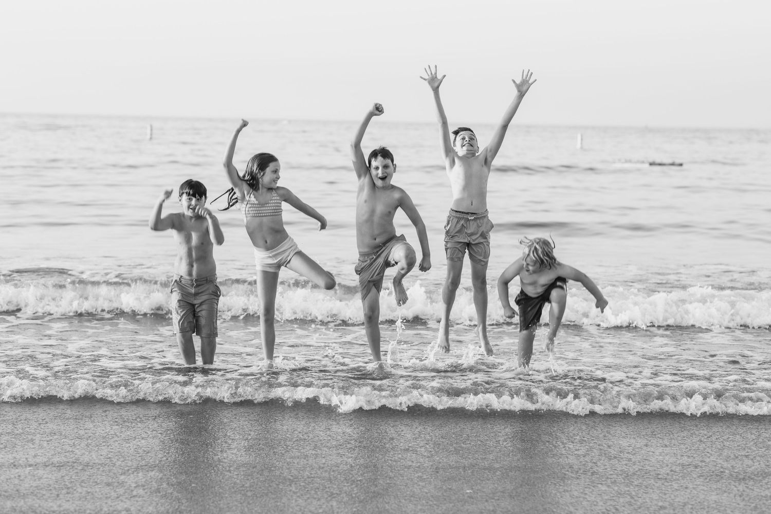 Group playing and splashing in ocean waves at sunset on a sandy beach.