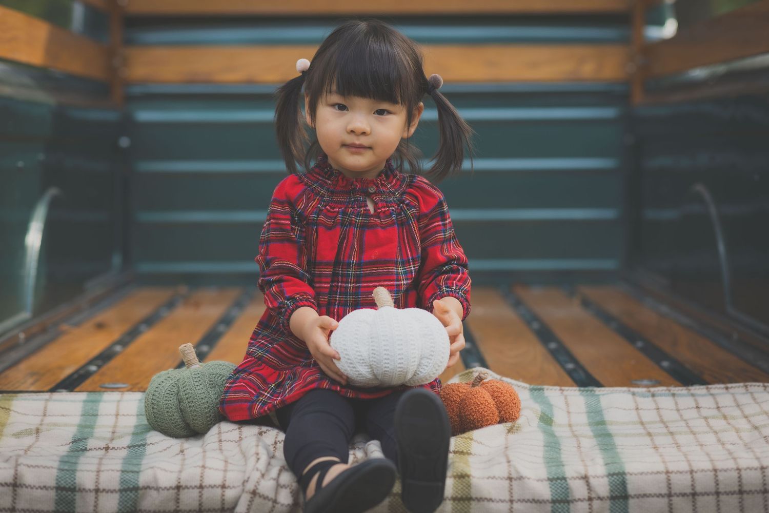 Child in plaid shirt sitting on striped cushion with bowl.