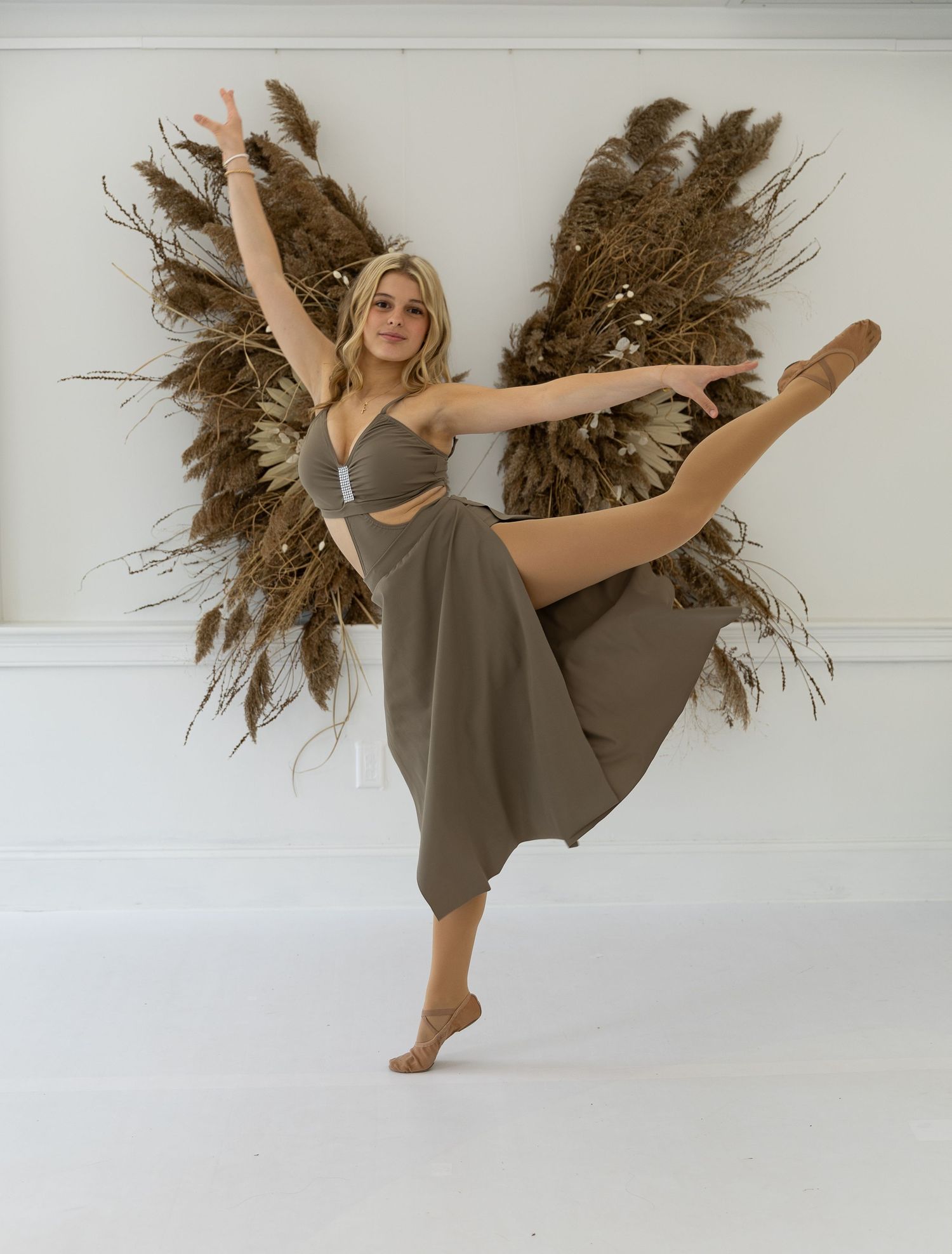 Dancer in grey dress performing dynamic movements with dried pampas grass decor.
